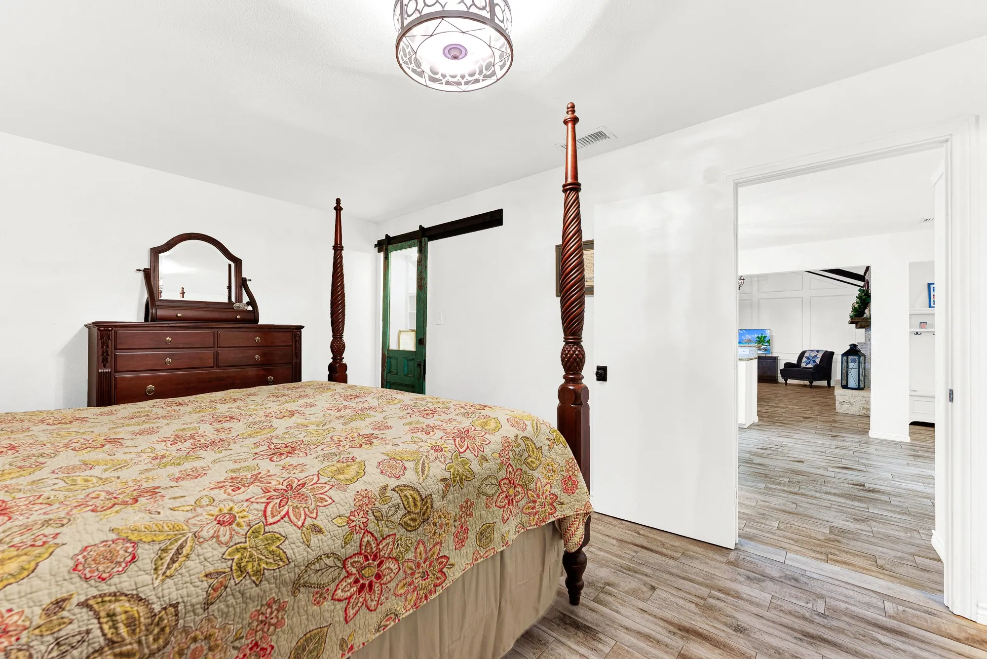 A wide, light-filled doorway opens directly into the main living spaces, giving the owner's sanctuary a connected yet private feel. Wood-look tile flooring stretches seamlessly throughout the room, pairing low-maintenance durability with high-end style.