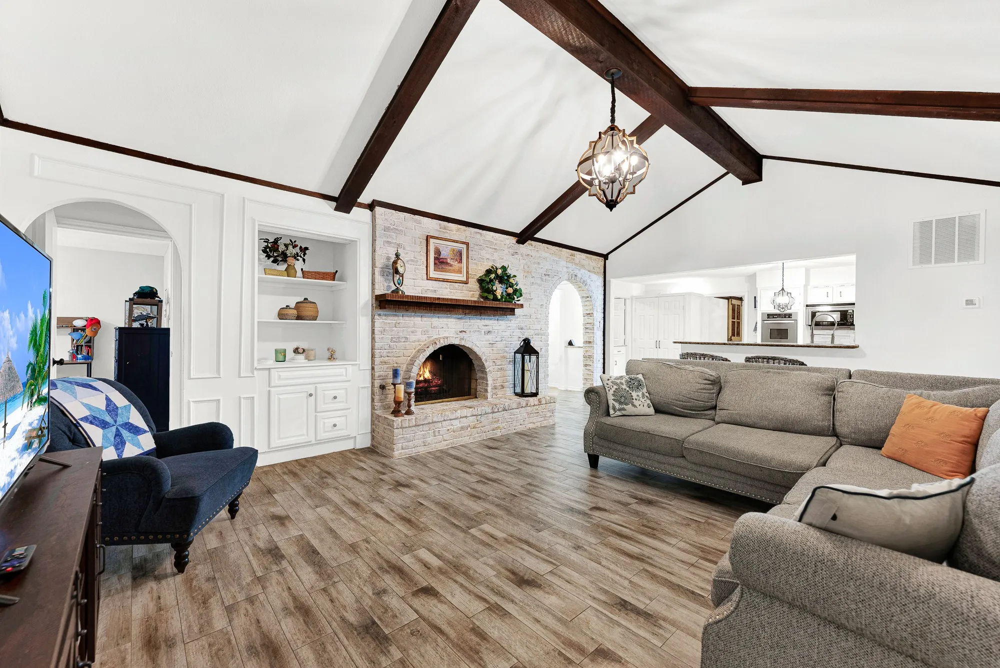 This view centers on the whitewashed brick fireplace with its rustic mantle, flanked by built-in cabinetry and open archways. Imagine curling up on cool evenings near a crackling fire while enjoying the warm, character-filled ambiance.