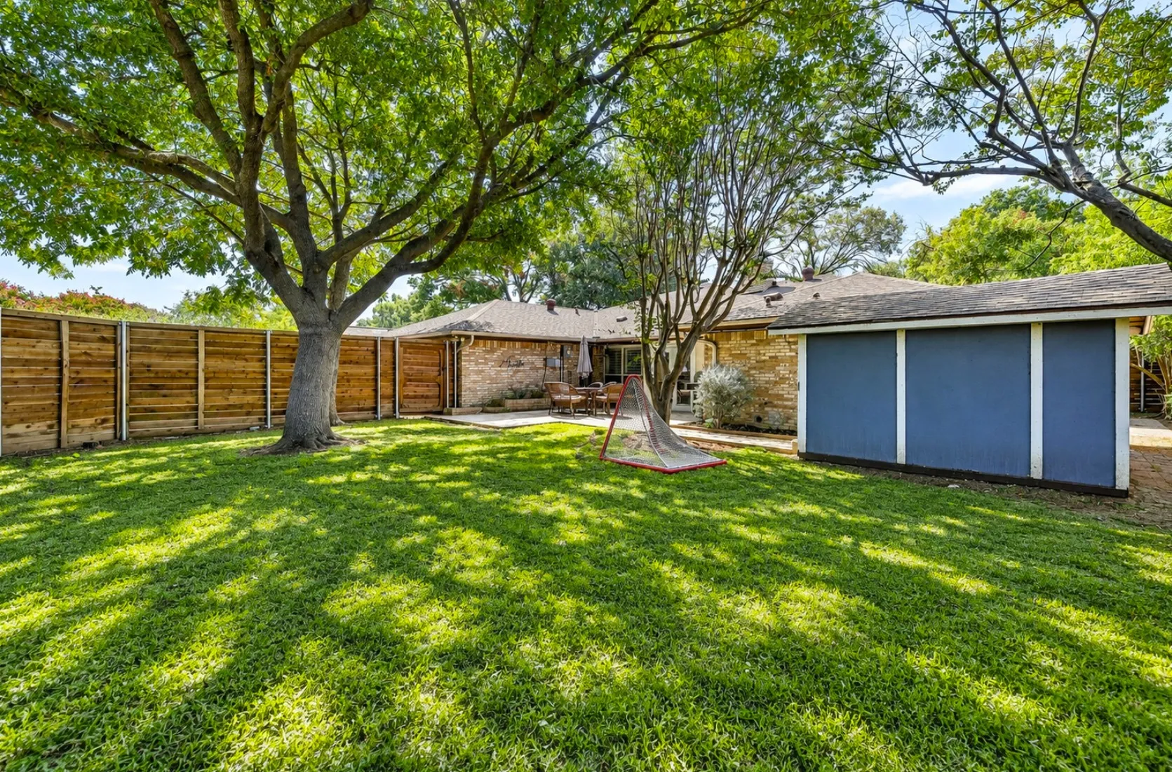 A tall, horizontal board-on-board wood fence fully encloses the yard for maximum privacy and peace of mind. Generous open grounds beneath a towering tree canopy leave plenty of room for play, gardening, or future backyard projects. Digitally enchanced by AI.