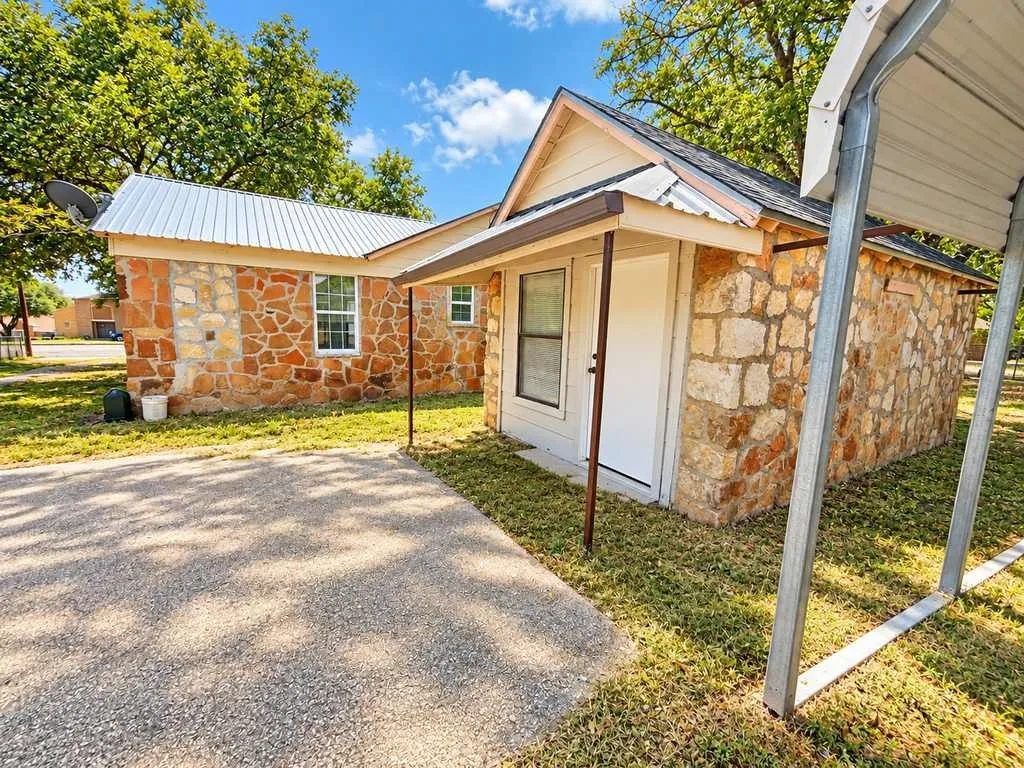 Covered exterior entry and concrete area beside the stone main home.