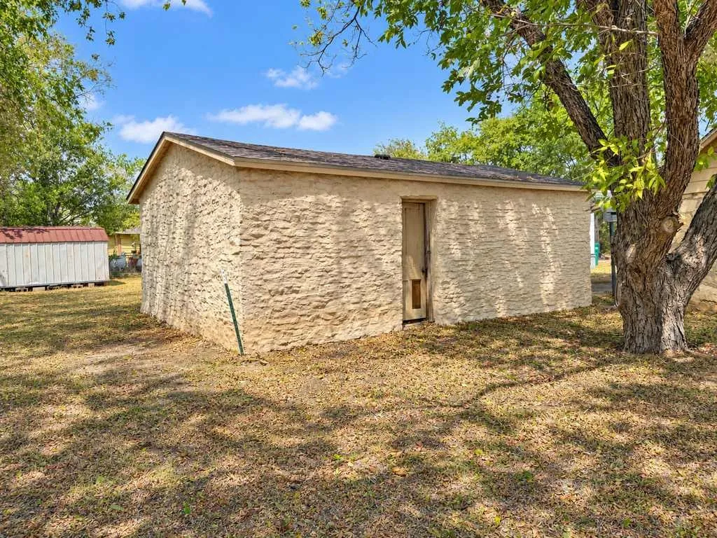 Detached outbuilding with a separate pedestrian entrance beside a mature tree.