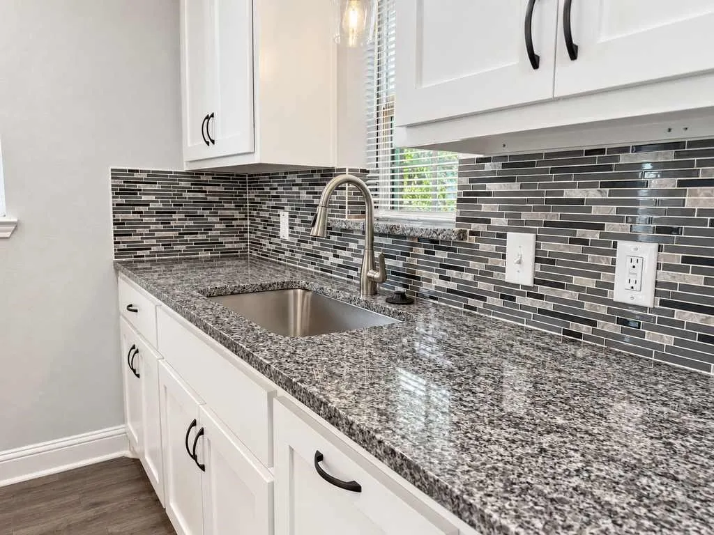 Main home kitchen sink, granite countertop, and tile backsplash.