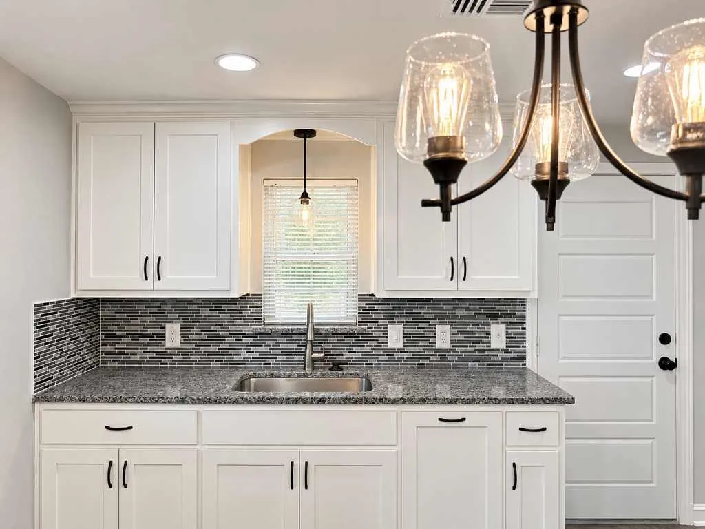 Main home kitchen with white cabinetry, granite countertops, tile backsplash, and pendant lighting.
