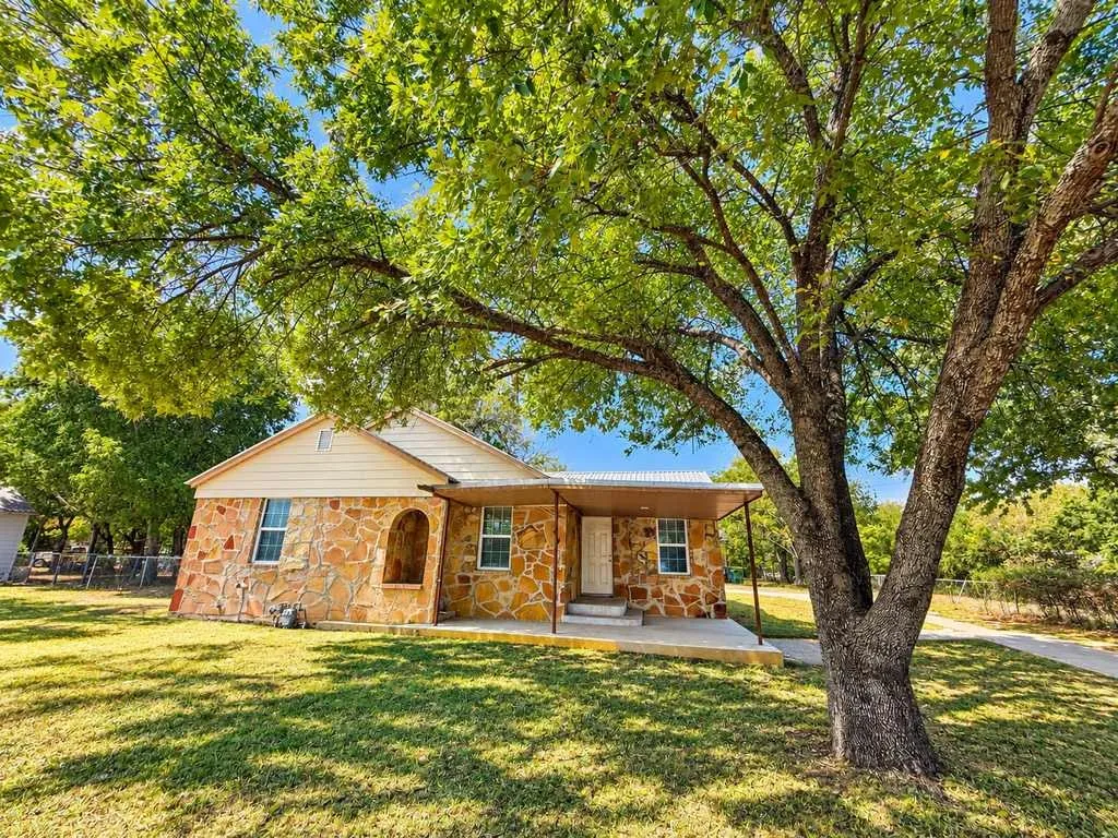 Stone main home beneath large shade trees at 1115 W. Main Street in Gatesville, Texas.