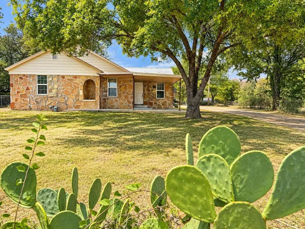 Stone main home framed by shade trees and cactus in Gatesville, Texas.