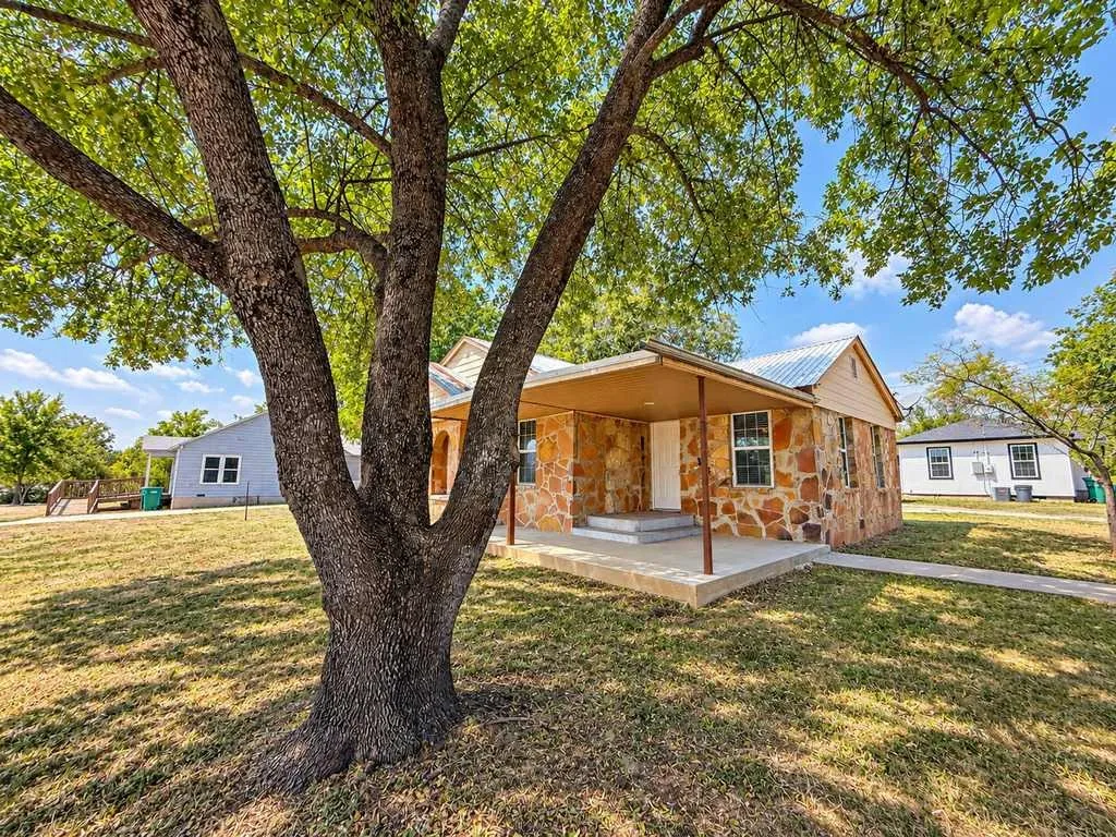 Main home tour begins here: covered front porch beneath a mature shade tree.