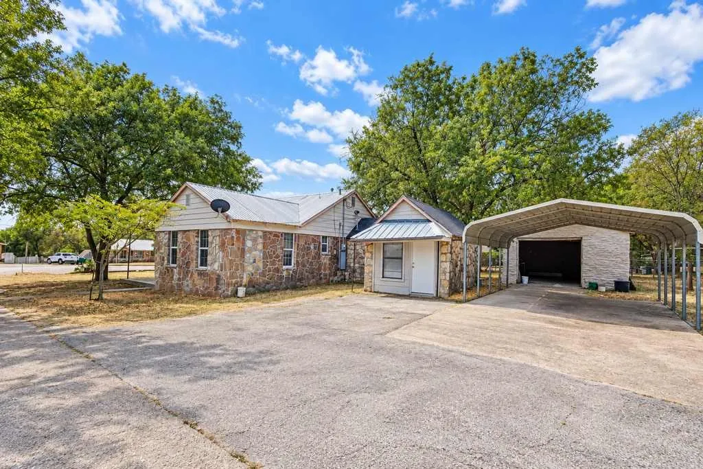 Concrete parking area, covered parking, and detached garage beside the main home.