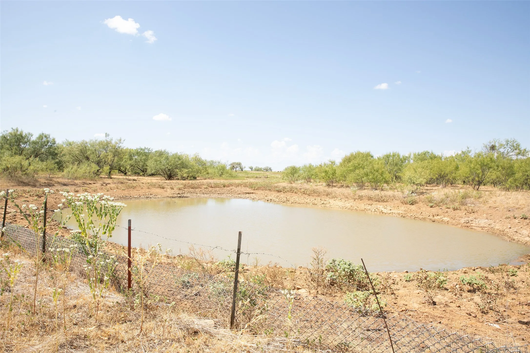 Pond featuring surrounding natural foliage and a partial perimeter fence