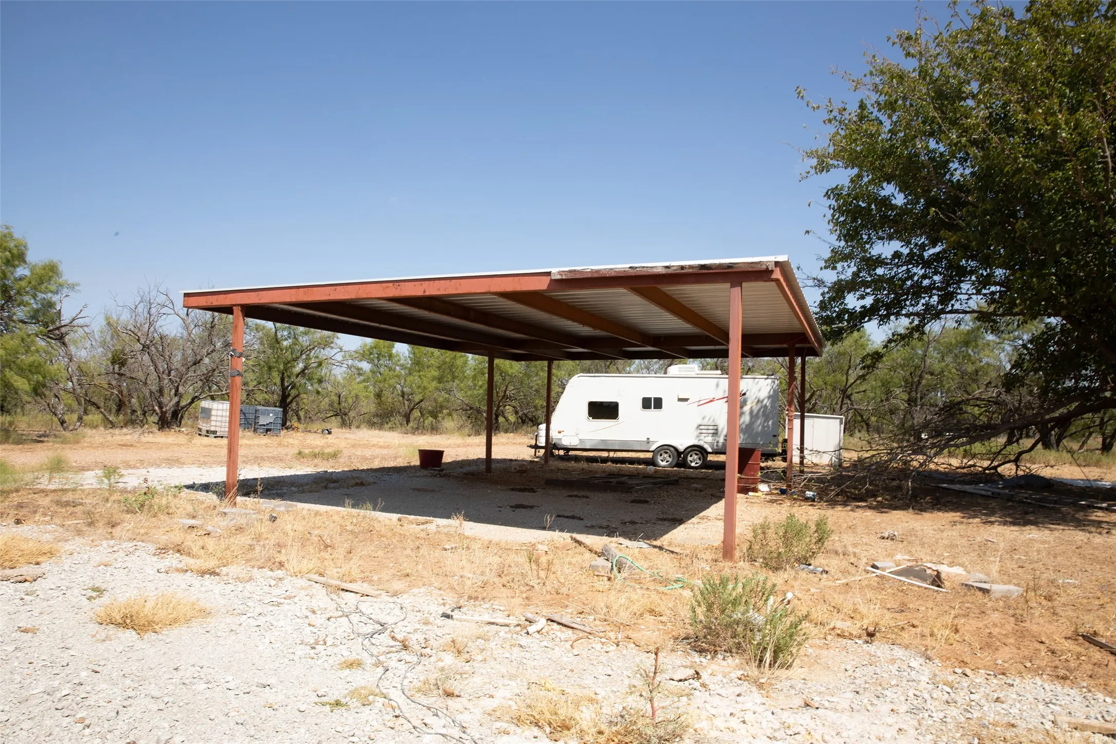 Metal carport structure with a corrugated roof over a gravel pad