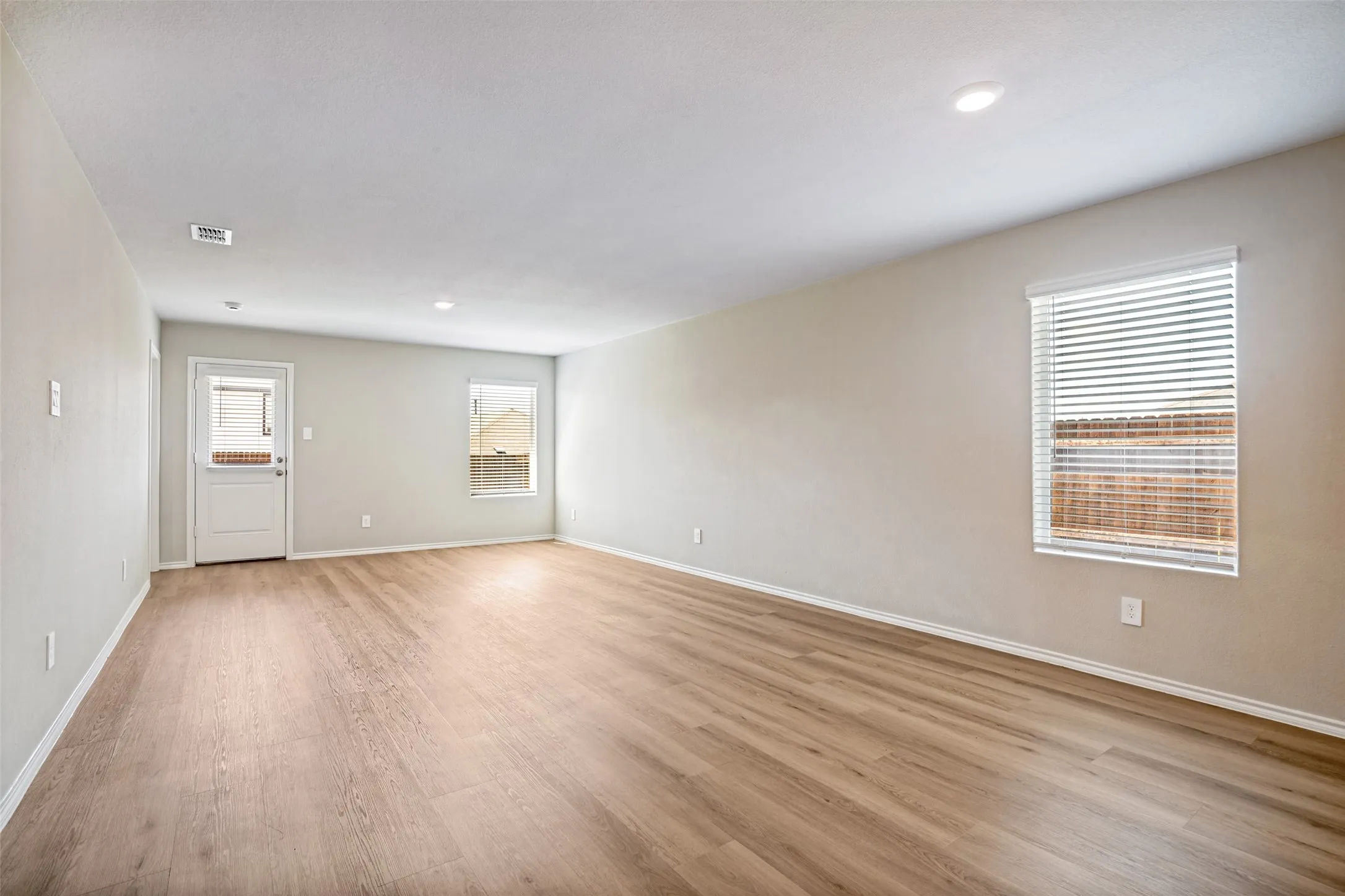 Spacious room featuring wood-finish flooring, neutral paint, multiple windows with blinds, and recessed lighting