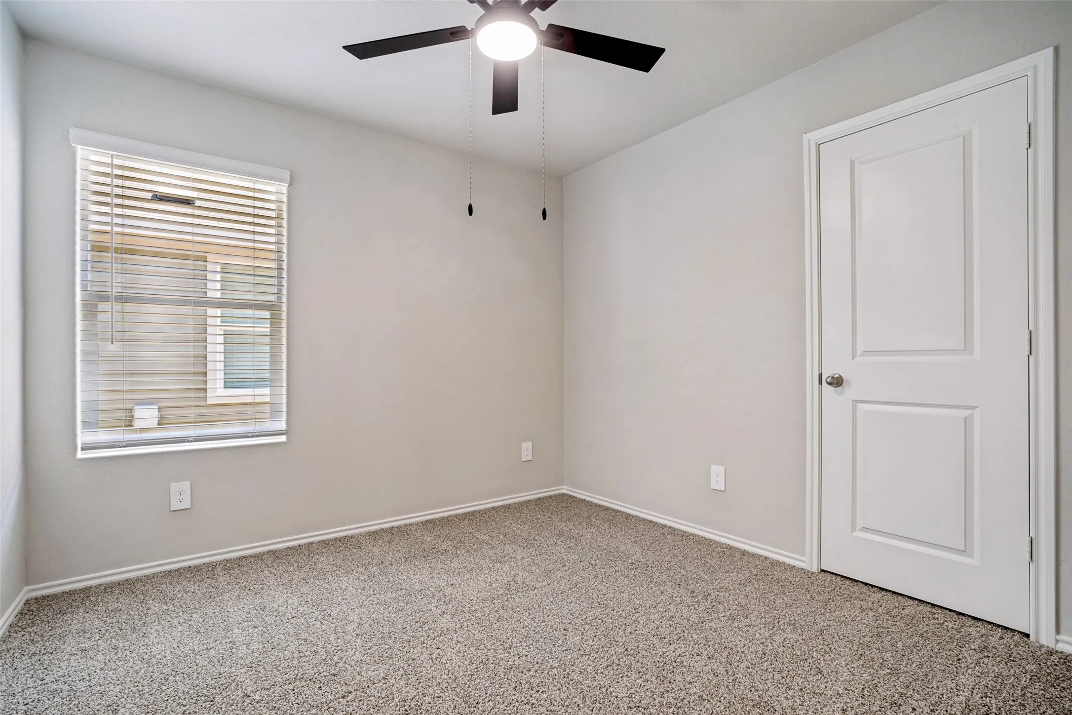 Neutral wall paint, textured carpet flooring, window with blinds, panel door, and a ceiling fan with integrated lighting