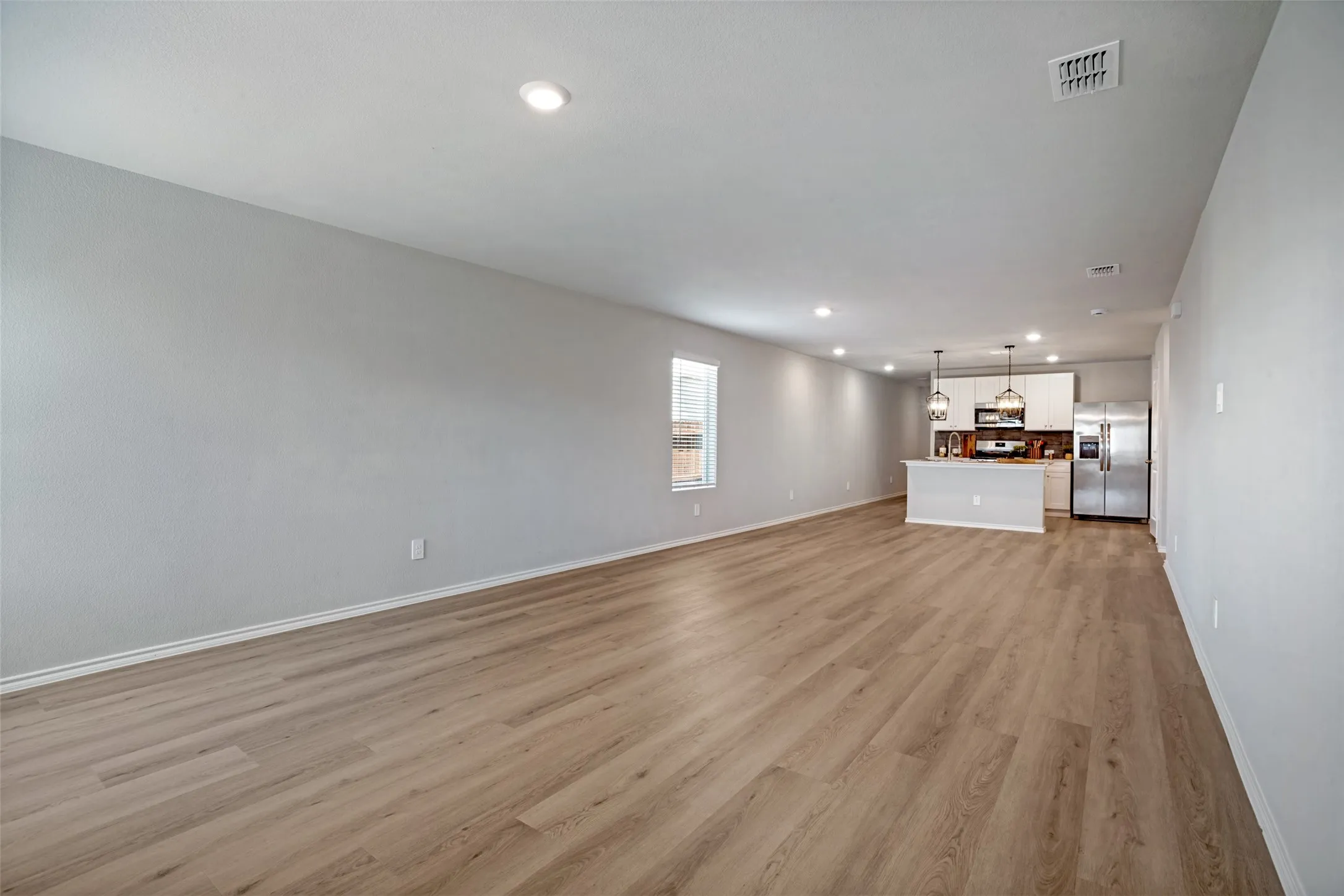 Open-concept living space featuring wood-finish flooring, recessed lighting, and a kitchen island with pendant lighting