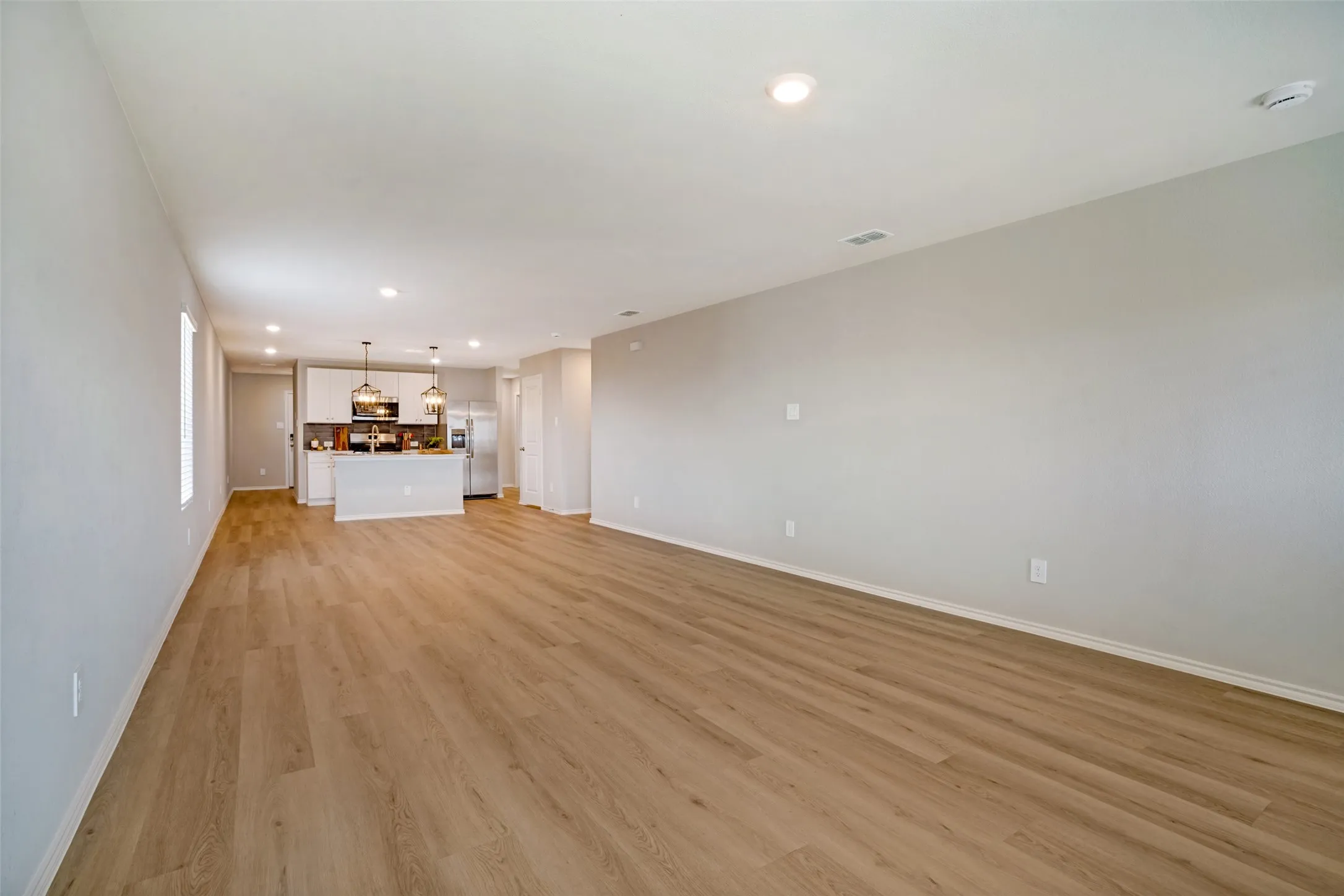 Open-concept living space with wood-finish flooring, recessed lighting, and a kitchen island with pendant lighting