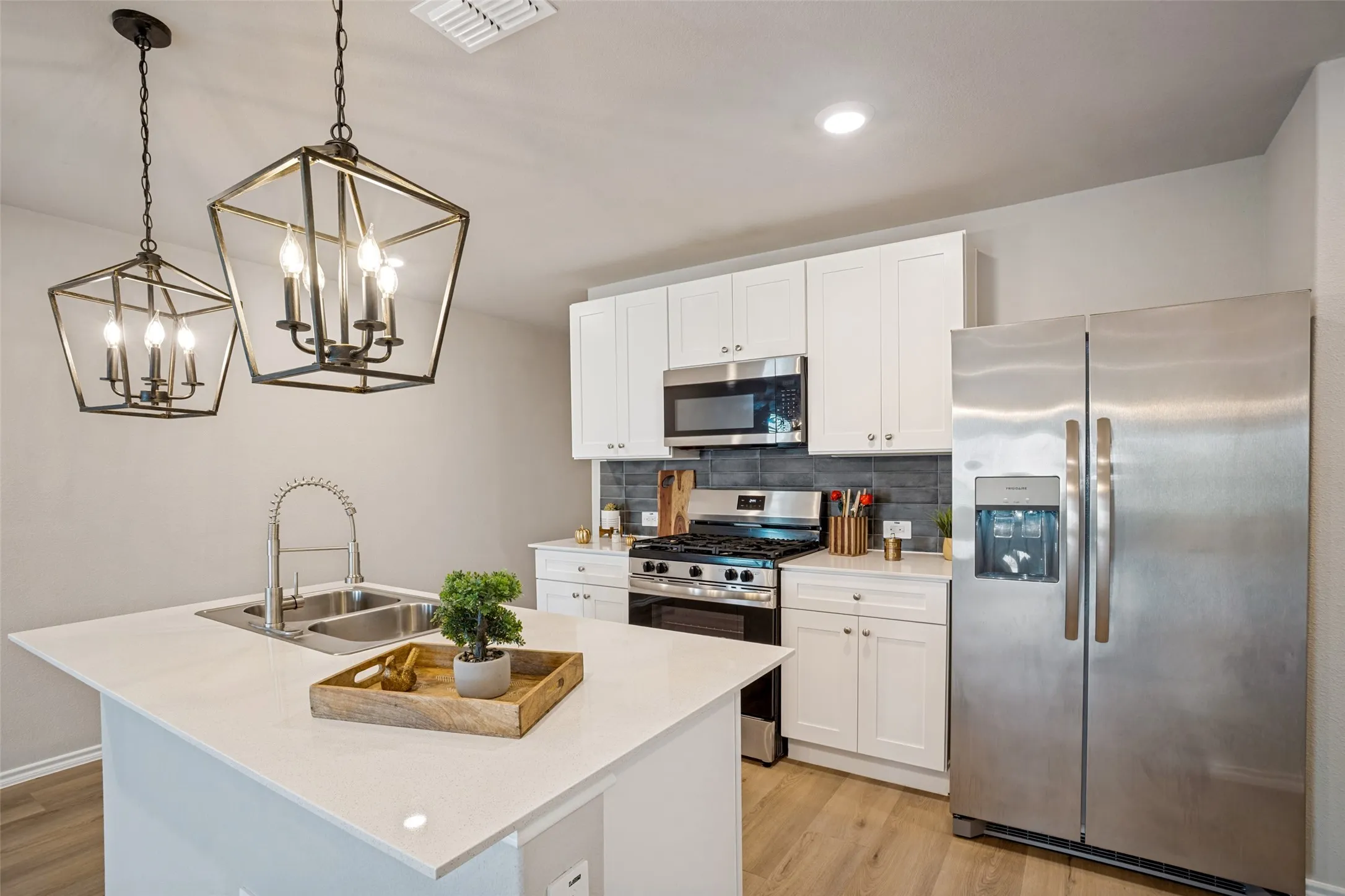 Kitchen featuring a central island with dual basin sink, white cabinetry, stainless steel appliances, and wood-finish flooring