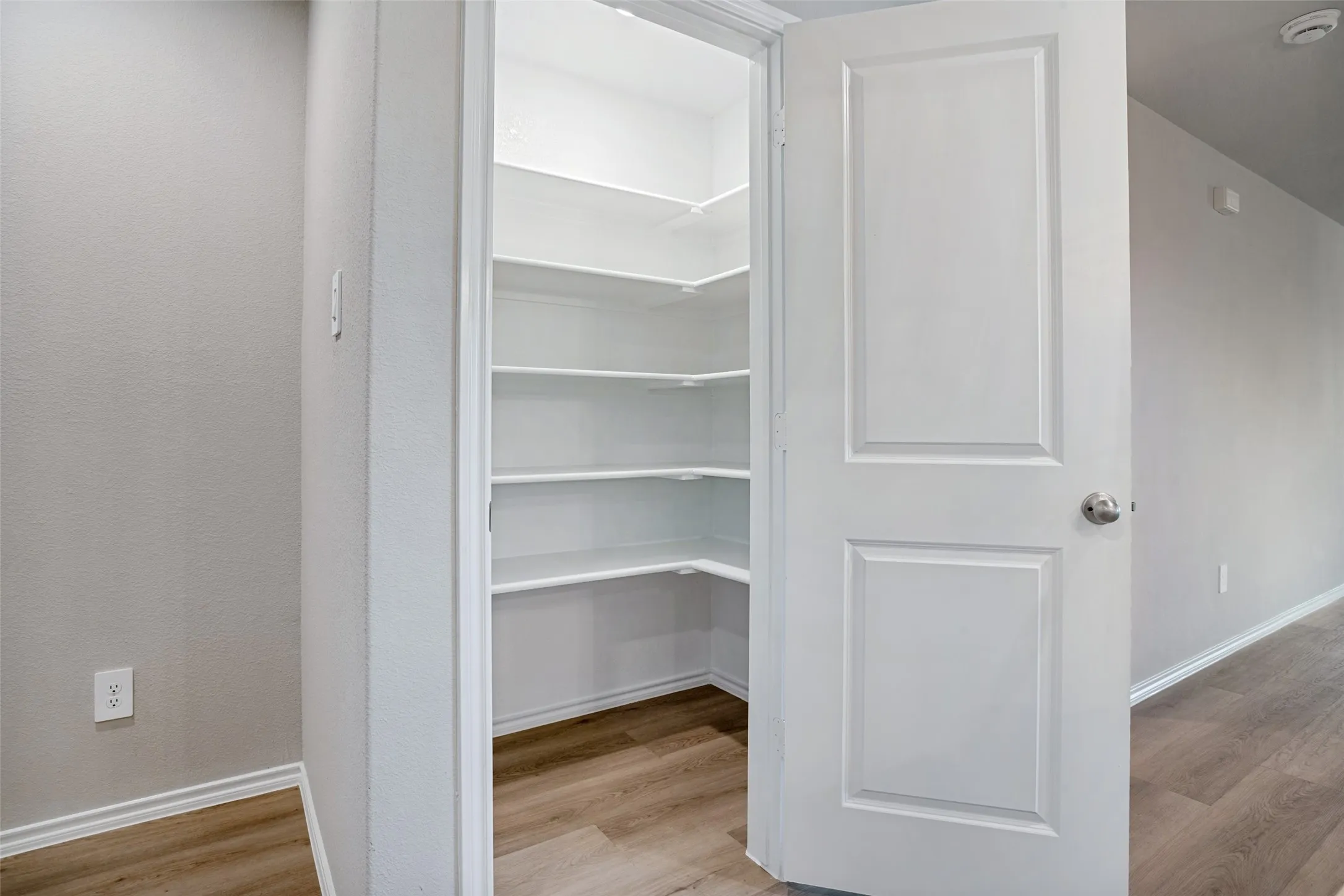 Corner pantry with multiple white shelves and wood-finish flooring