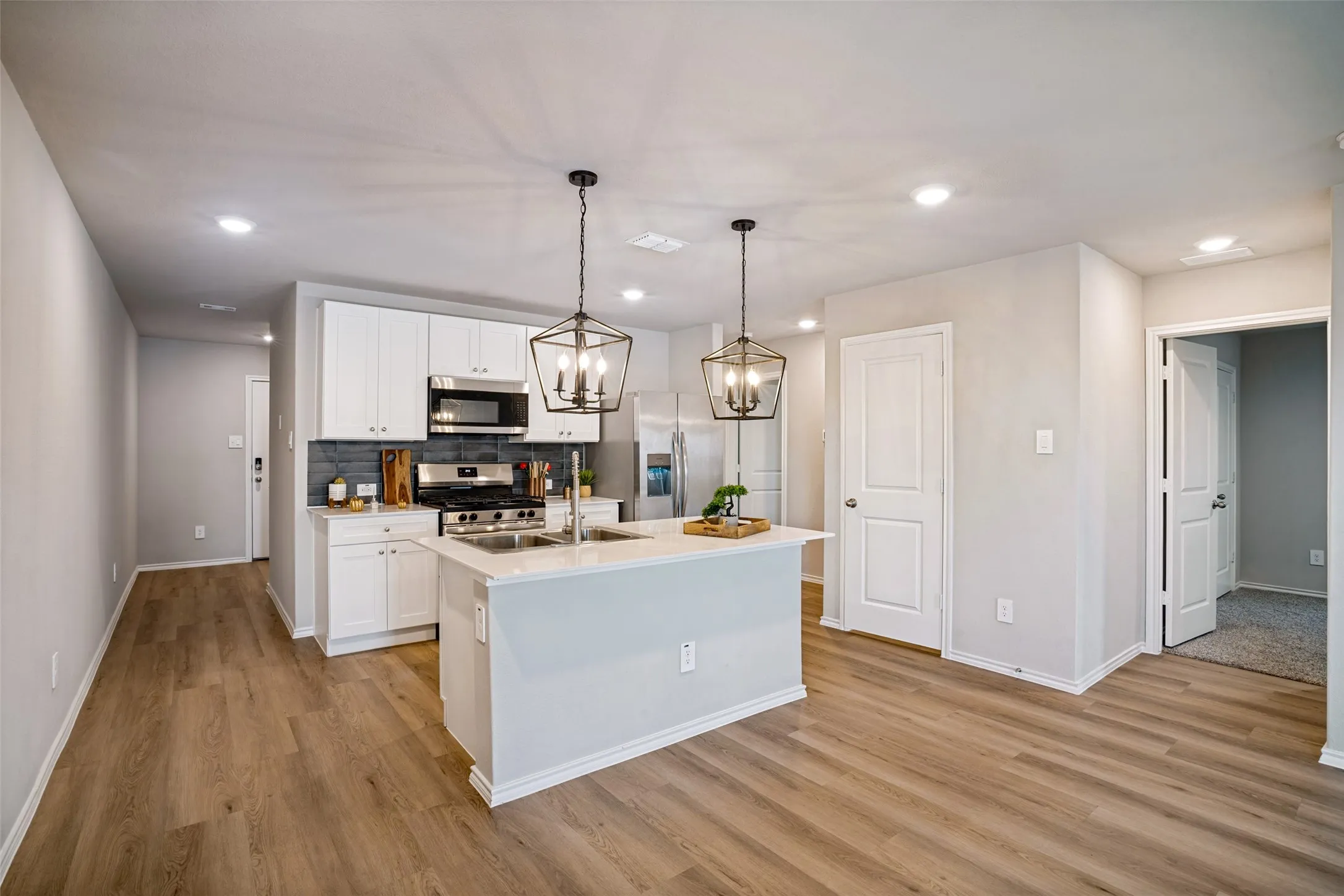 Kitchen featuring white cabinetry, stainless steel appliances, a center island with sink, and wood-finish flooring