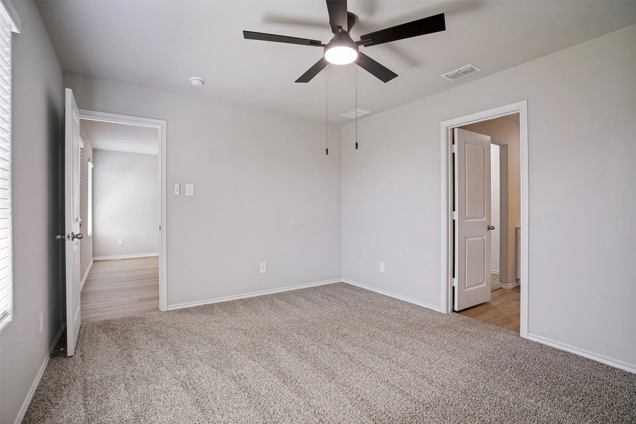 Spacious room with light gray walls, plush carpeting, and a ceiling fan with integrated lighting