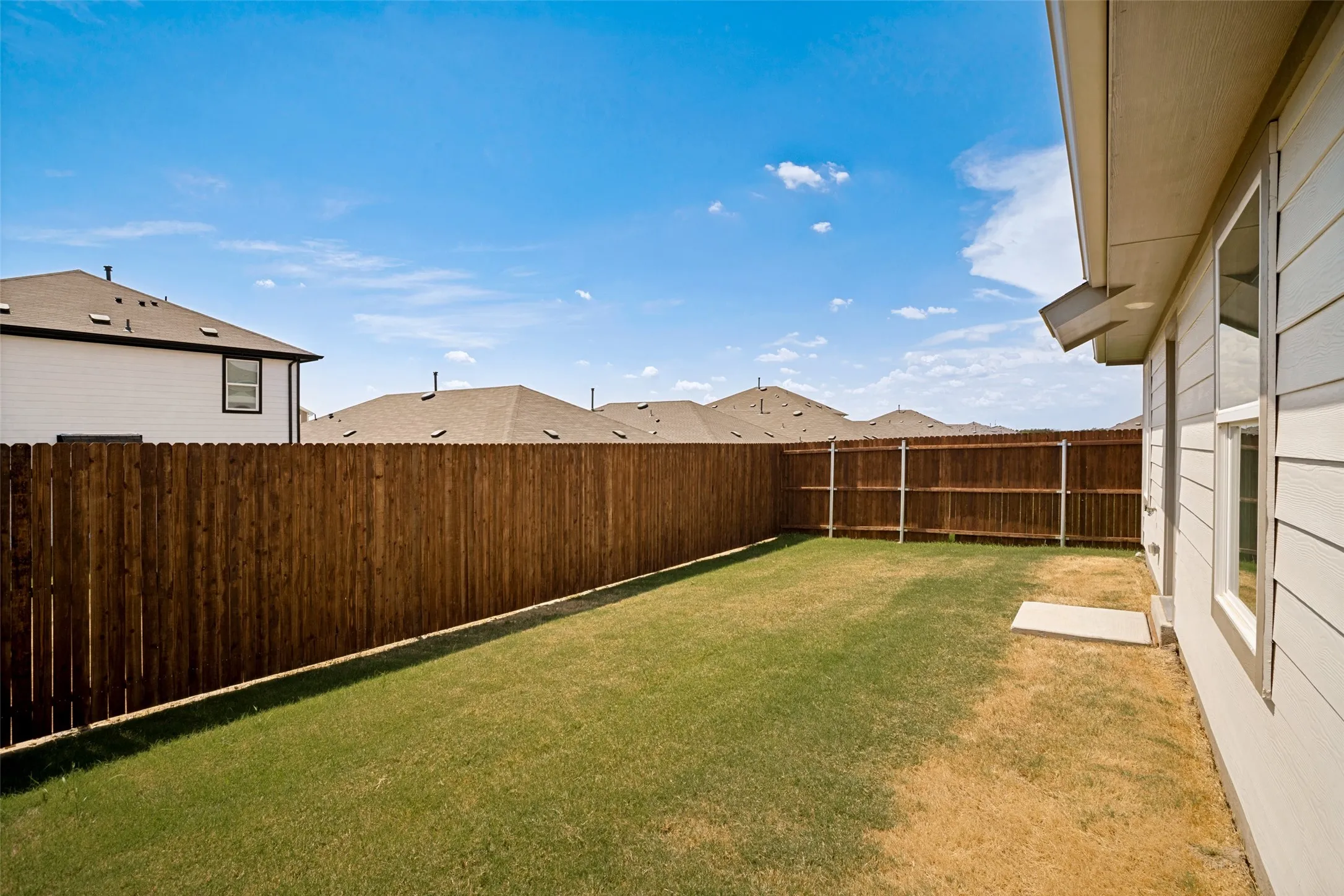 Private wood fencing encompassing a grass lawn and a concrete pad