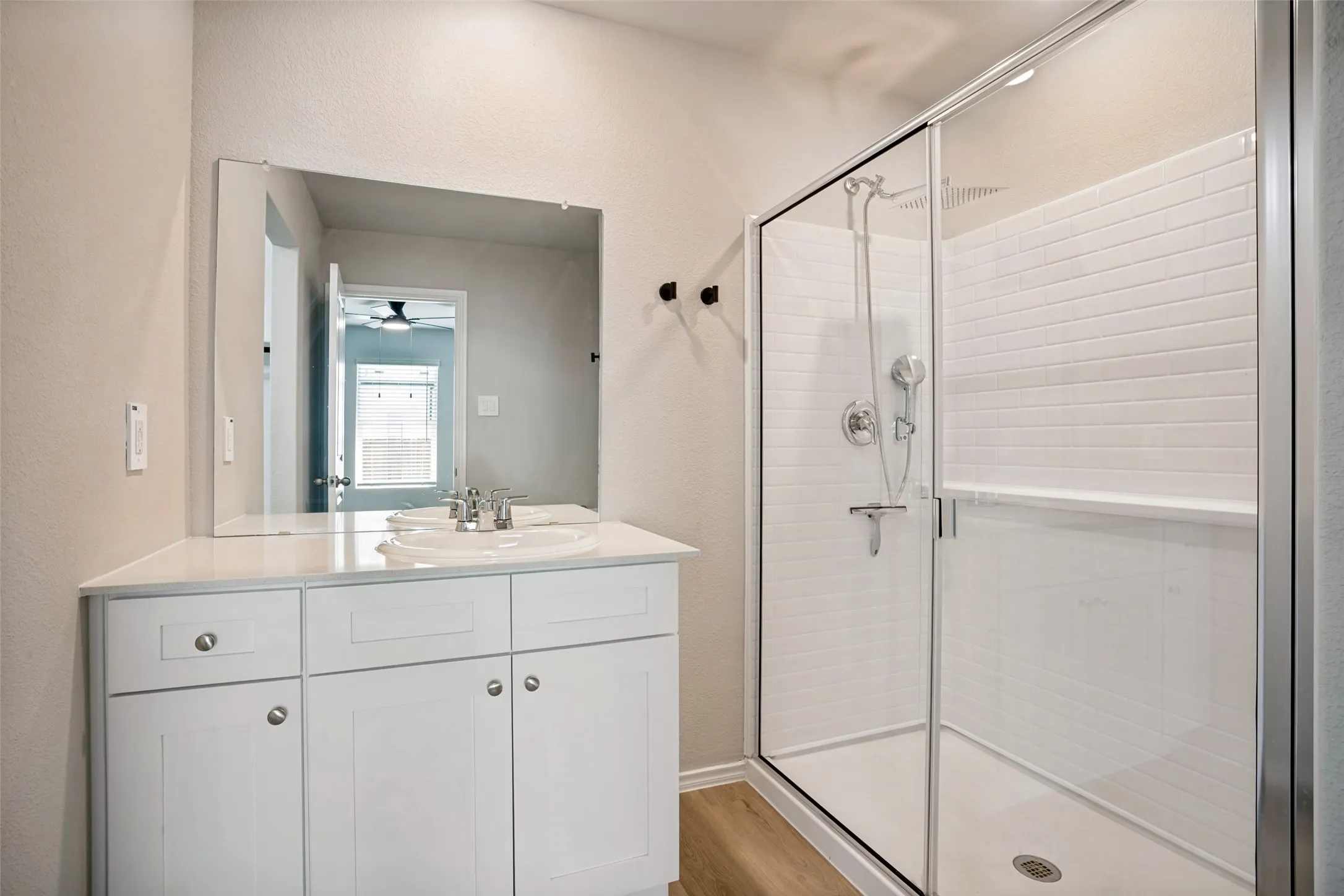 White shaker-style vanity with a double sink, expansive wall mirror, and a glass-enclosed shower featuring subway tile