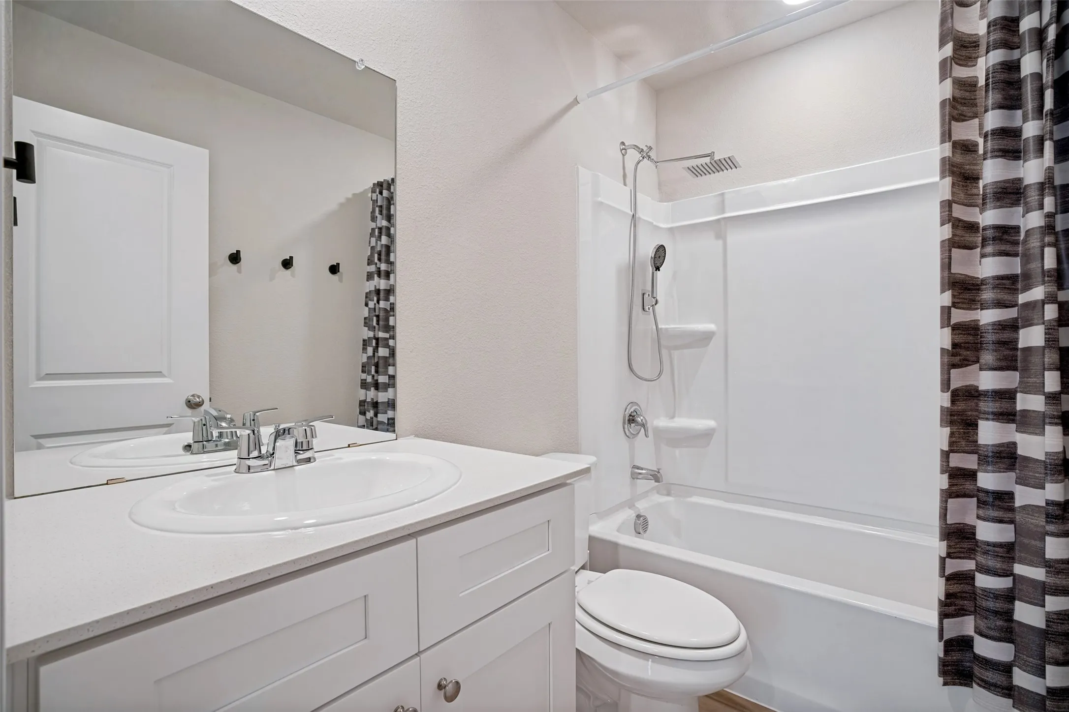 White vanity with an integrated sink and chrome faucet, large wall-mounted mirror, and a white bathtub with a shower/tub combination