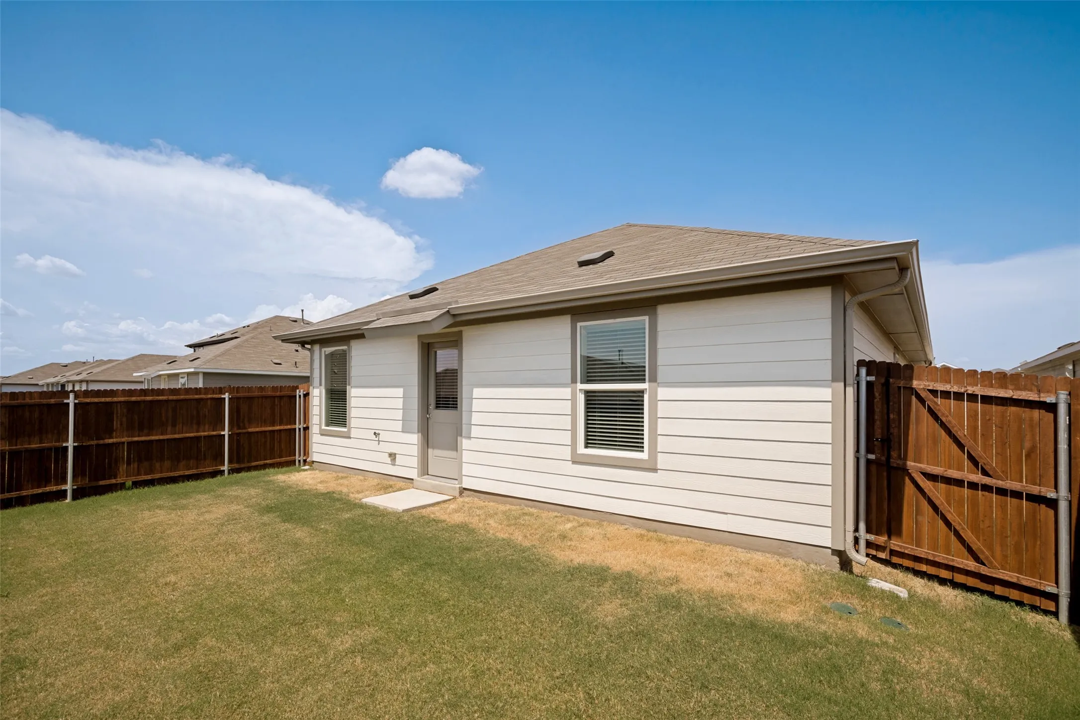 Expansive backyard featuring a partial wood fence, a light-colored siding exterior, and a side entry door