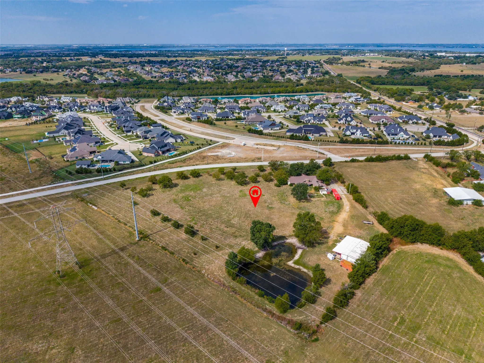 Expansive property featuring a private pond, multiple outbuildings, and open fields, with residential developments in the distance
