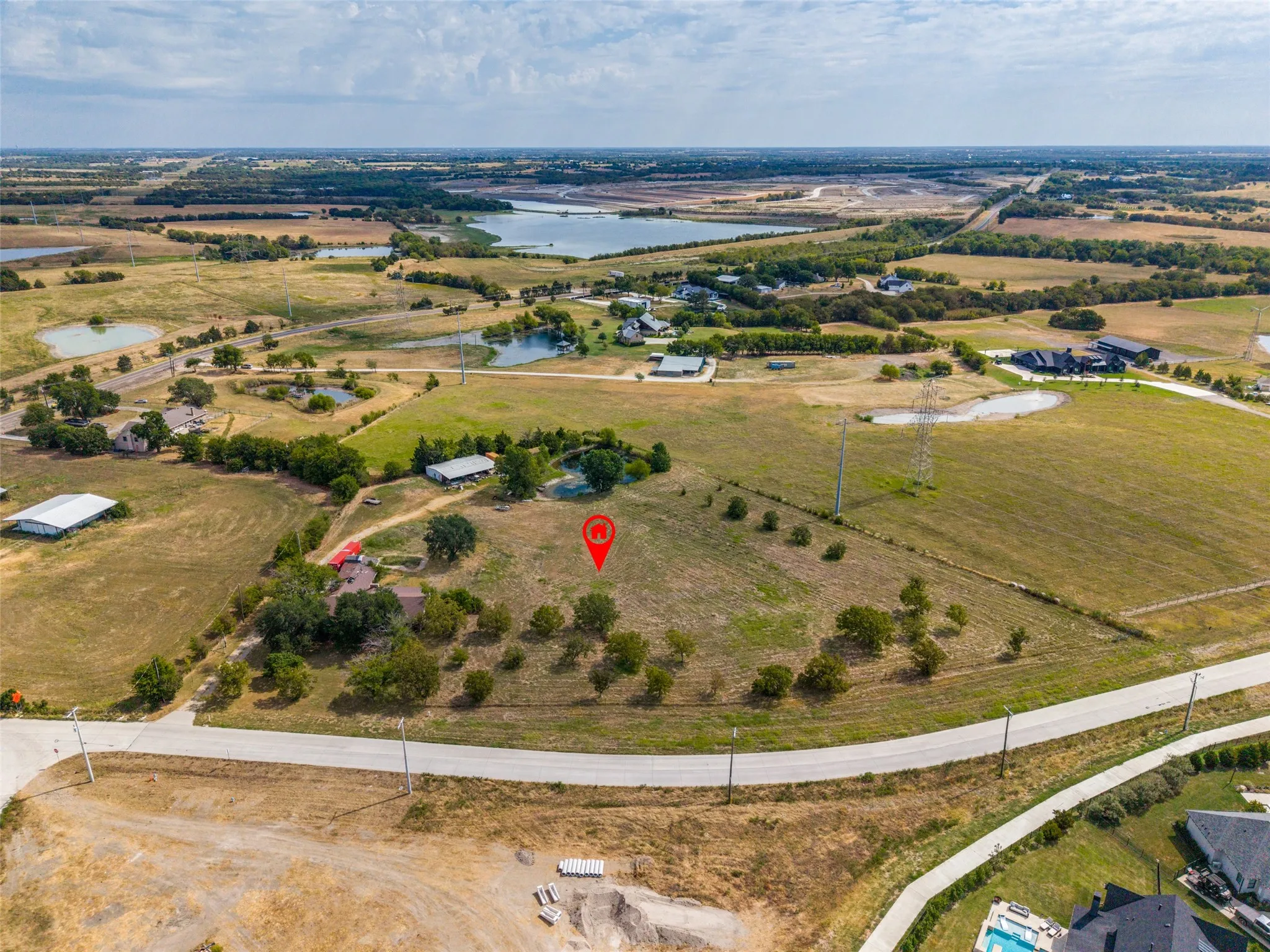 Expansive land with multiple bodies of water visible in the distance, featuring a paved road, and a mix of cleared and treed areas