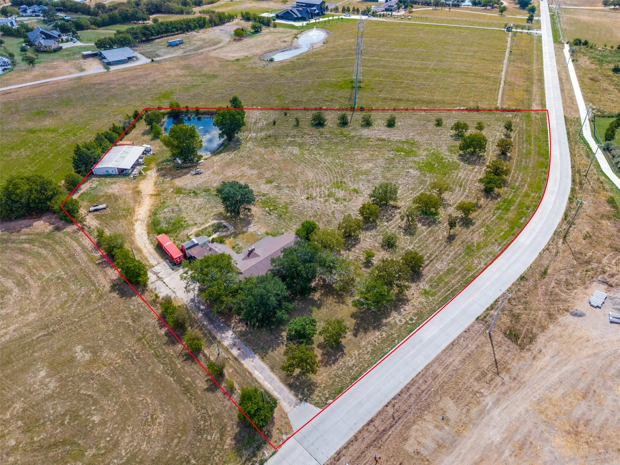 Expansive property featuring a private pond, mature trees, a detached structure, a curved paved road, and a single-story residence