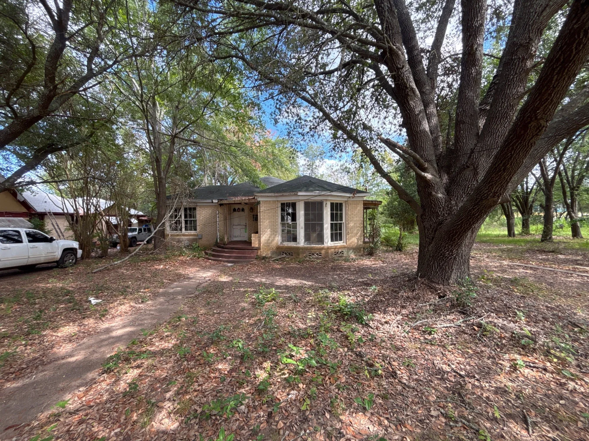 Front exterior view of the single-story home set back amidst mature shade trees and natural grounds.
