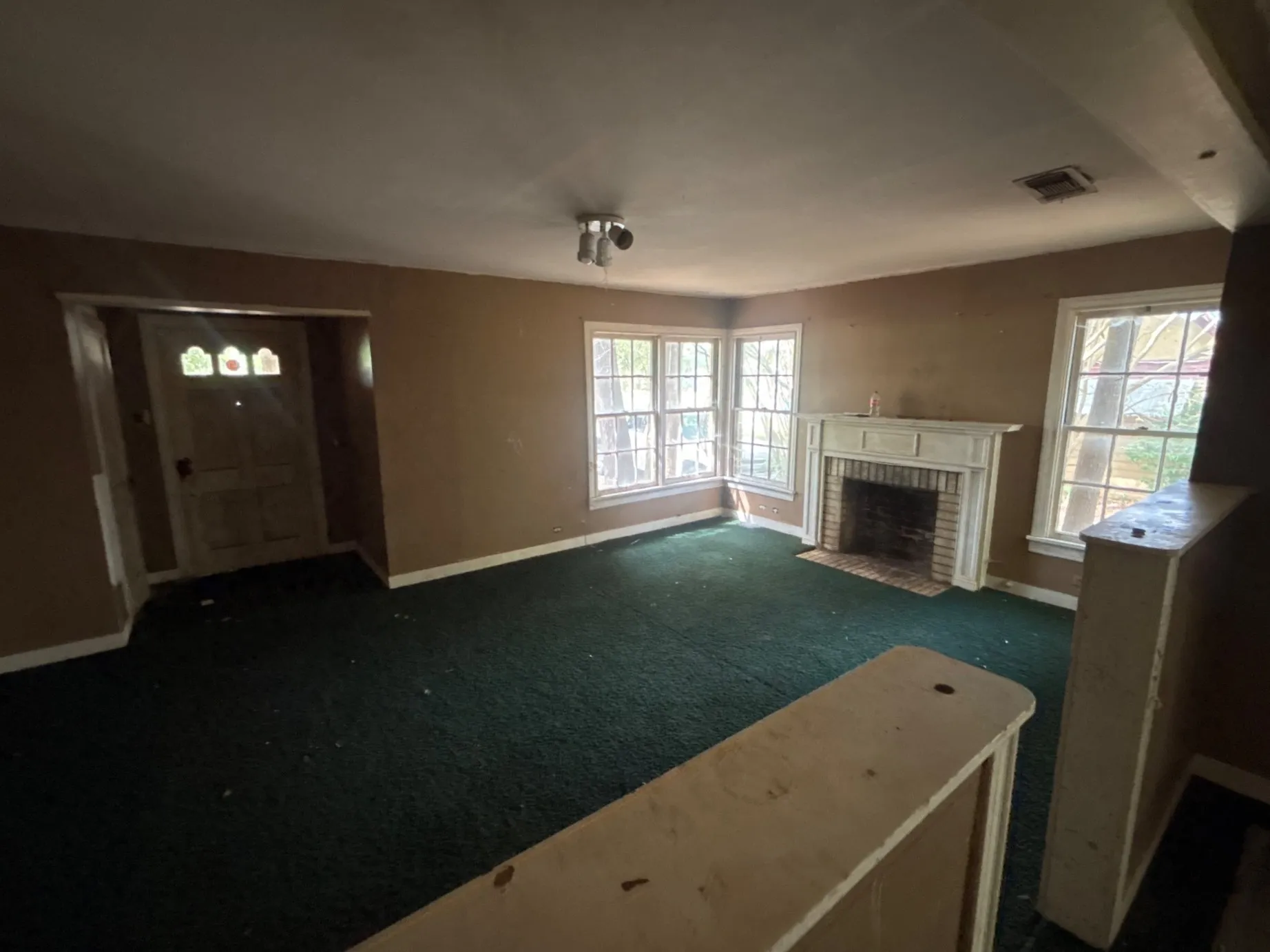 Spacious main living room featuring a cozy fireplace, ceiling fan, carpeted flooring, and front door entry access.