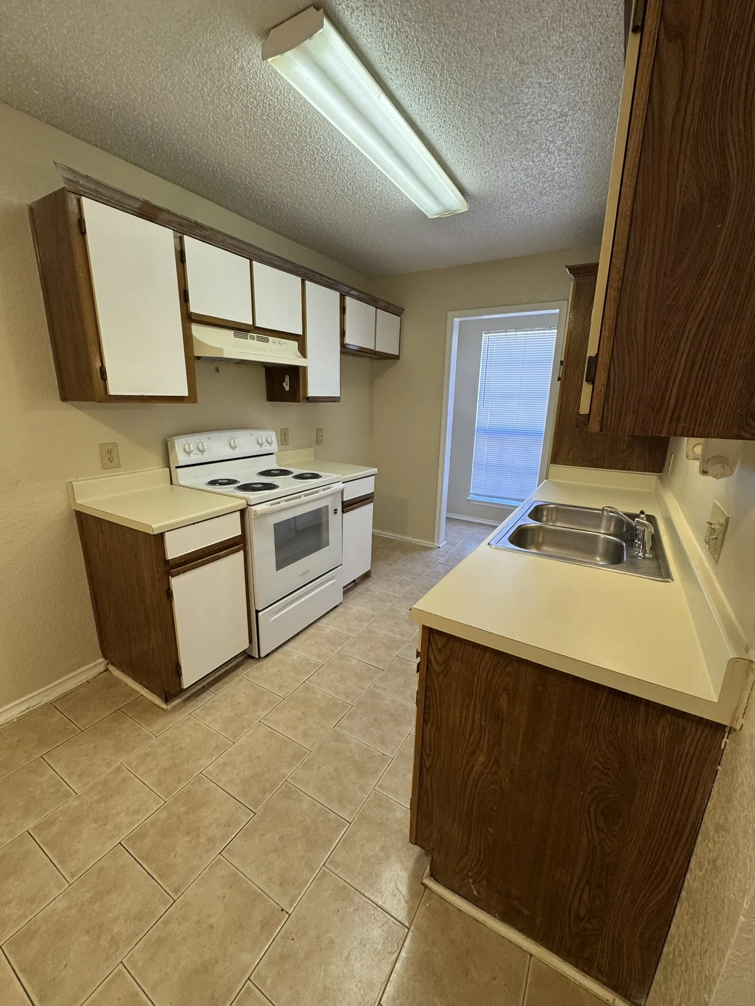 Kitchen featuring a double basin stainless steel sink, wood-finish cabinetry, light-toned countertops, ceramic tile flooring, and a range with an overhead exhaust fan