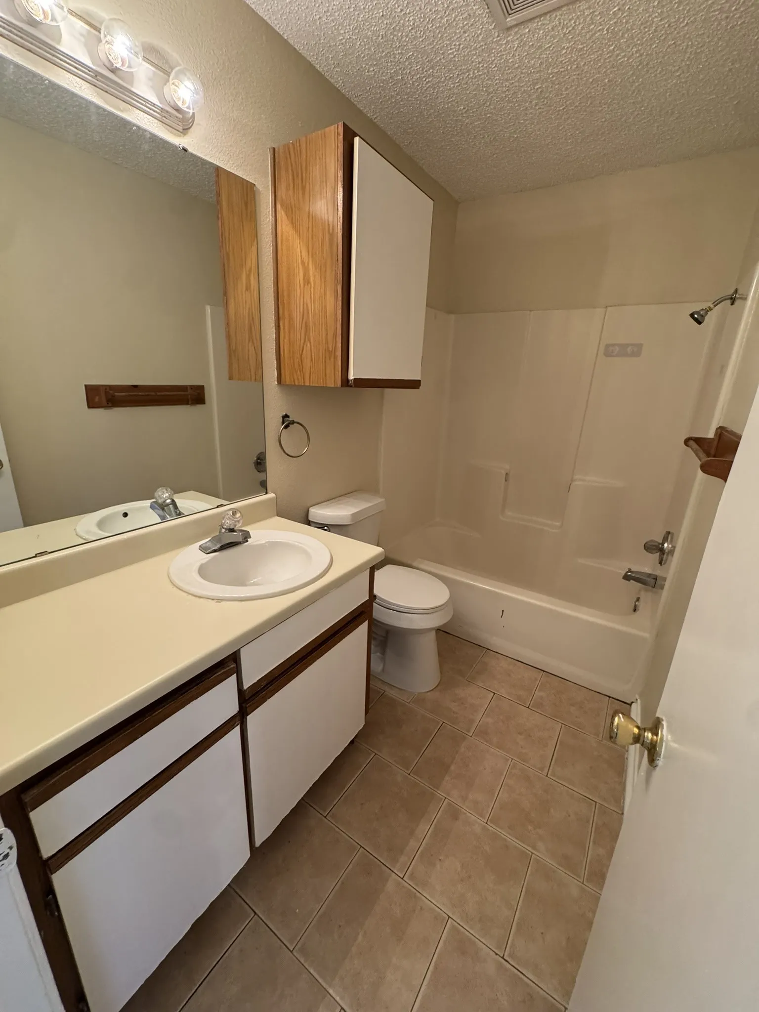 Vanity with integrated sink, wood-finish cabinetry, above-mirror lighting fixture, and tile flooring