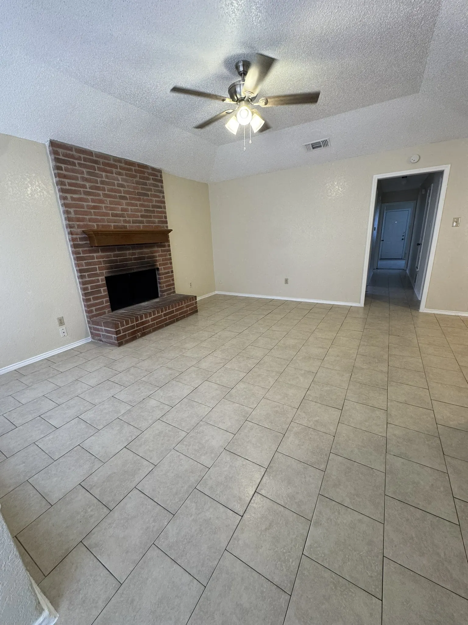 Brick fireplace with wood mantel, ceiling fan with integrated lighting, and tile flooring