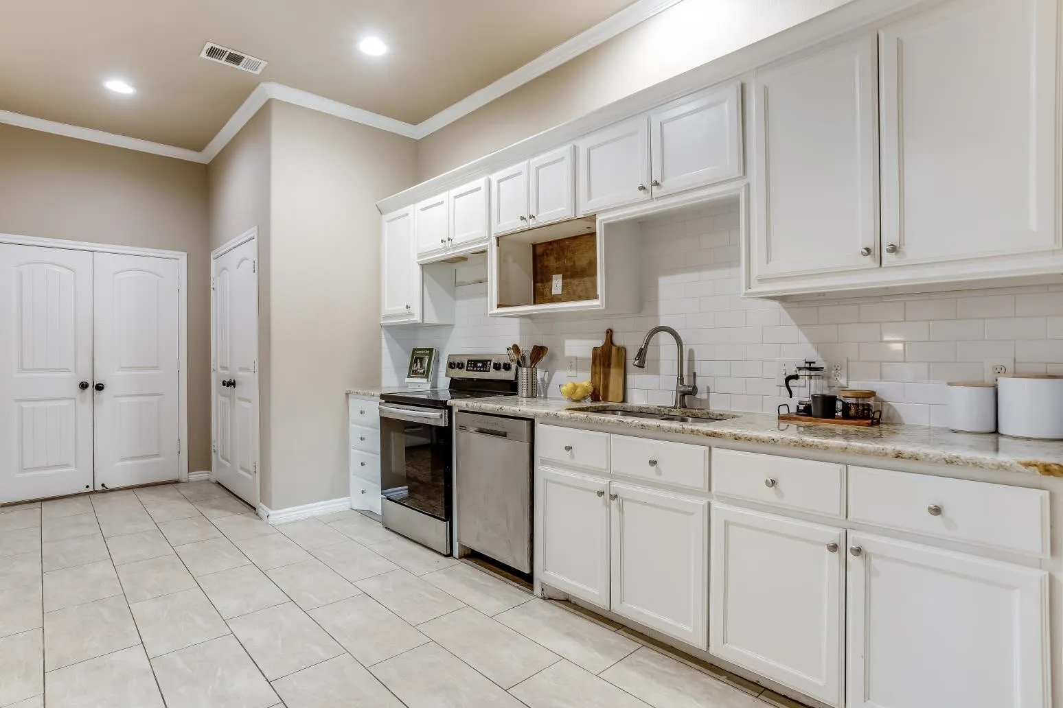 White shaker-style cabinetry, subway tile backsplash, stainless steel appliances, speckled stone countertops, and tile flooring