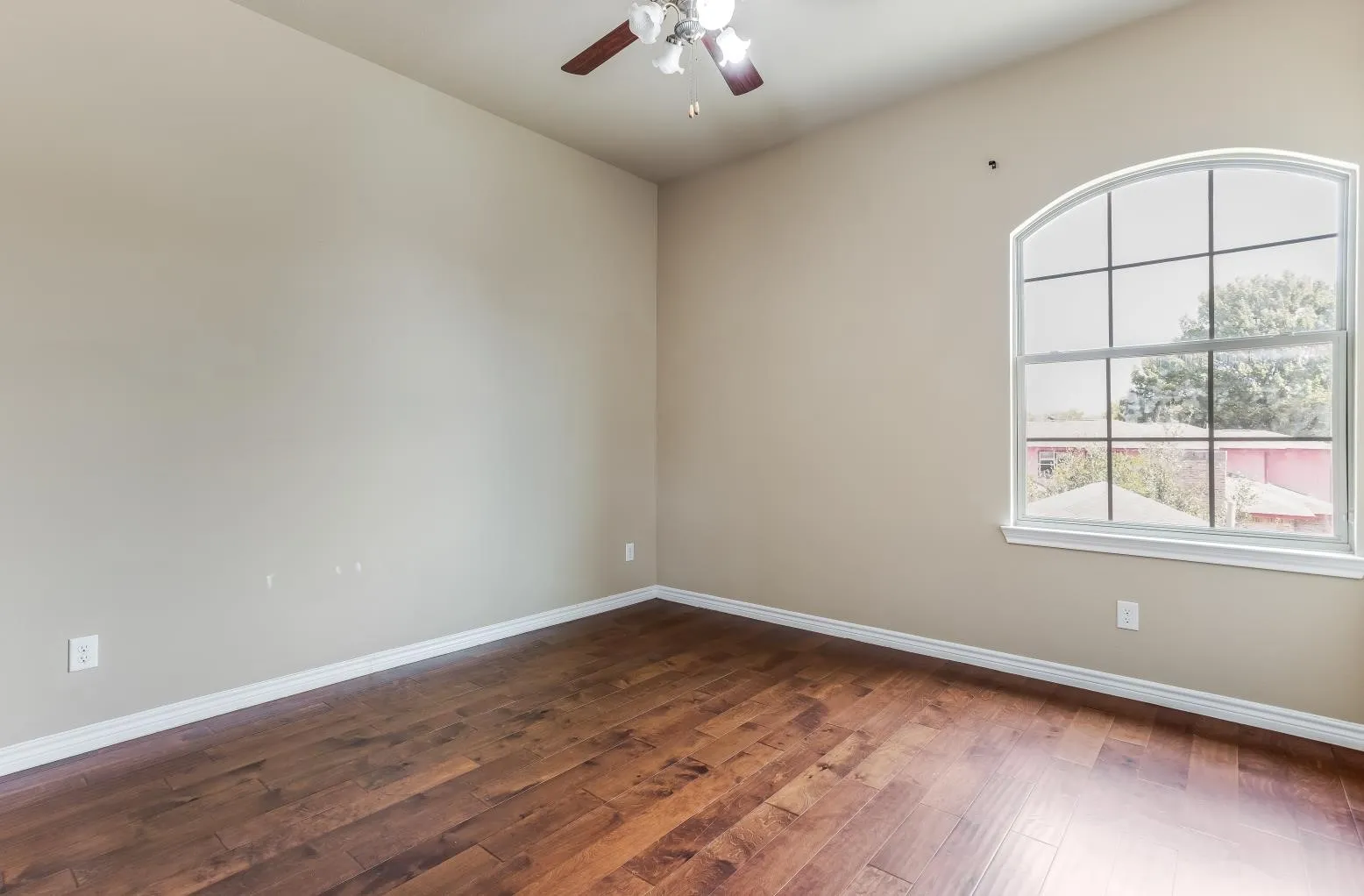 Wood-finish flooring, arched window, ceiling fan, and neutral wall tones