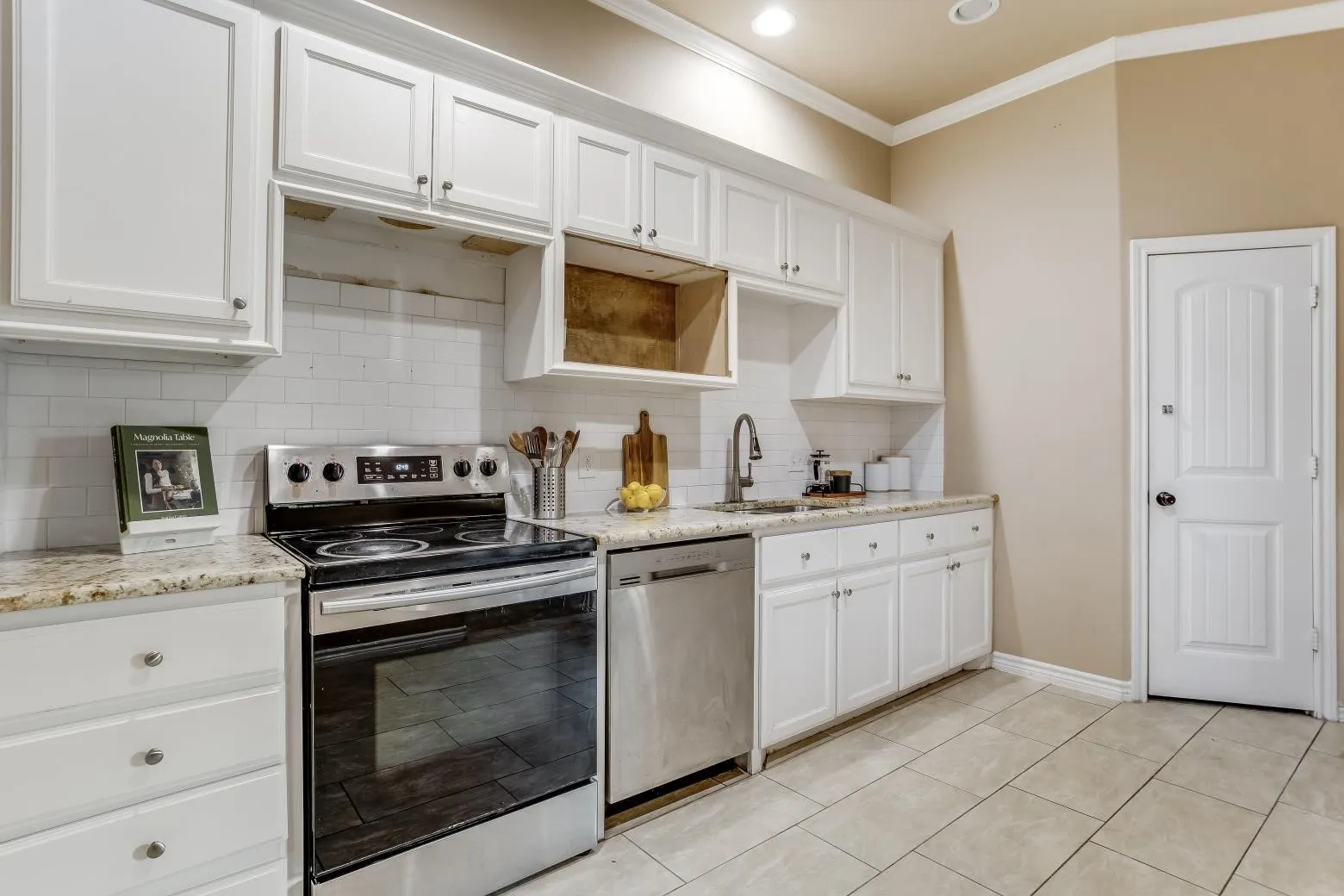 White cabinetry with silver-tone hardware, stainless steel range, stainless steel dishwasher, light-toned countertops, and subway tile backsplash