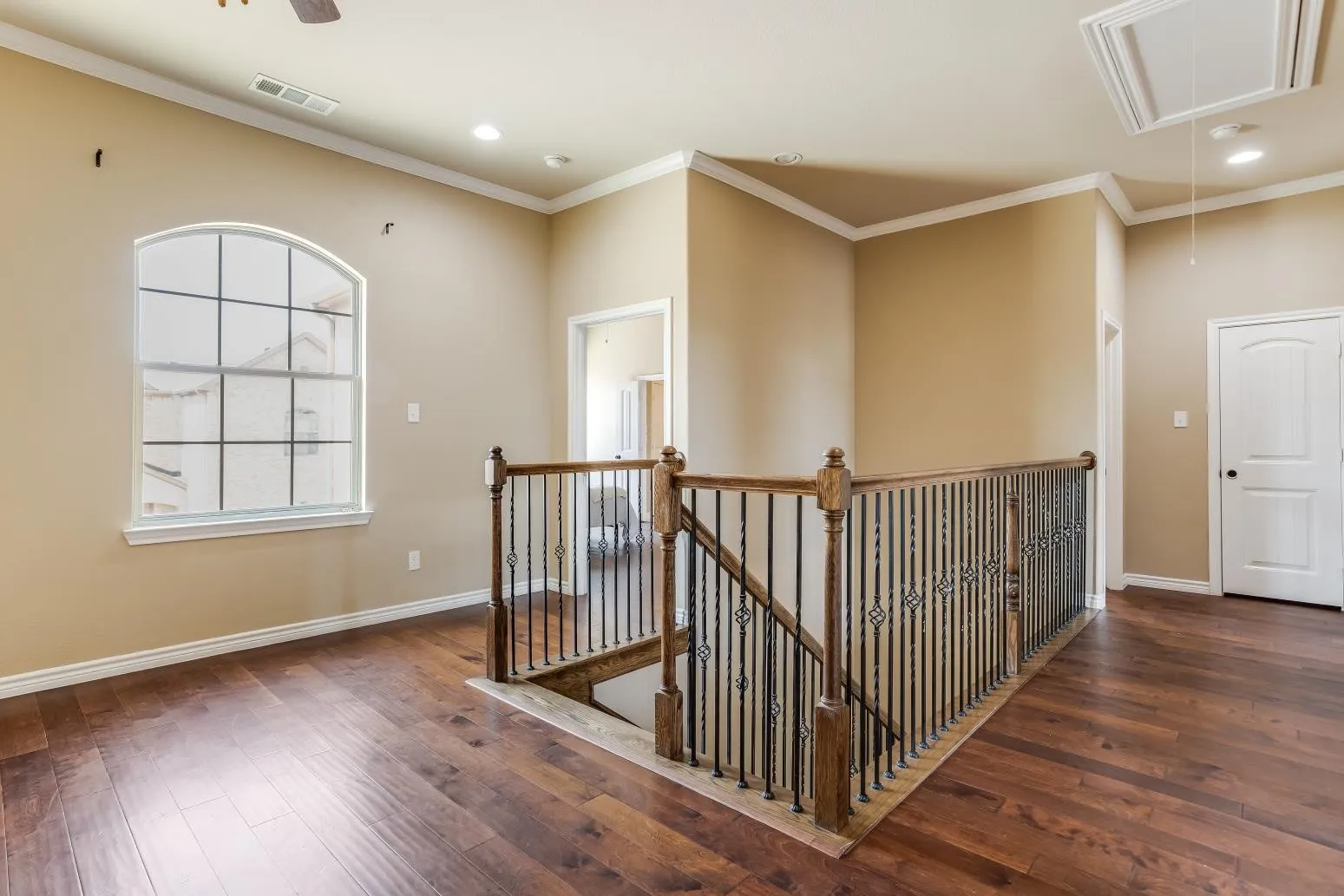 Arch-top window with grid pattern, wood-finish flooring, wrought iron and wood staircase railing, crown molding, and recessed lighting