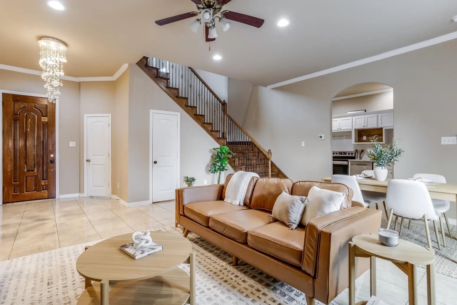 Recessed lighting throughout, tile flooring, wood-finish staircase with white risers, and an arched doorway leading to the kitchen