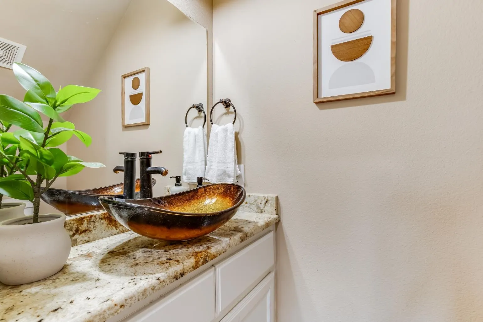 Granite countertop vanity with a vessel sink, dark bronze faucet, and white cabinetry