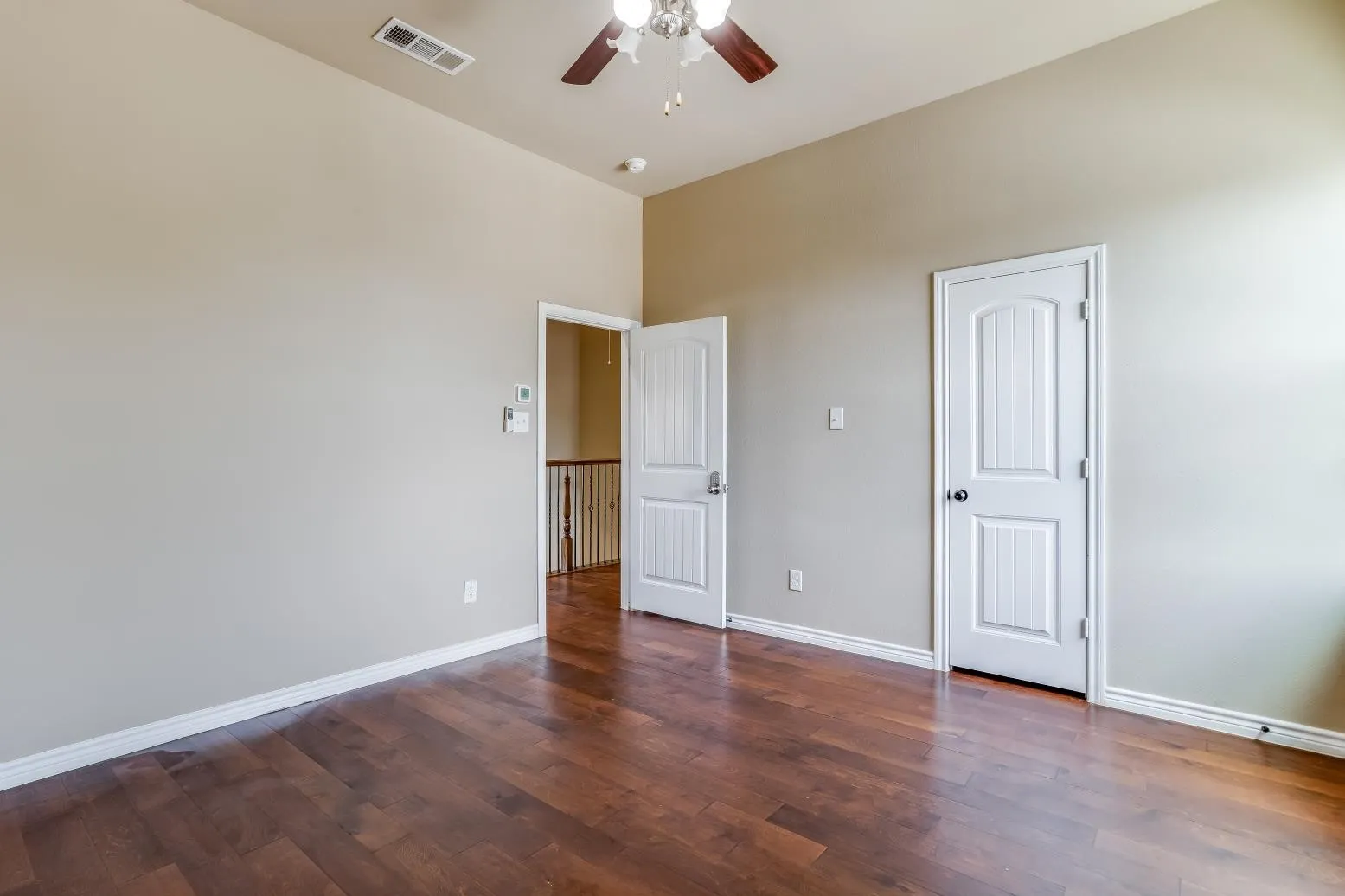 Wood-finish flooring, neutral wall tones, ceiling fan with integrated lighting, and white paneled doors