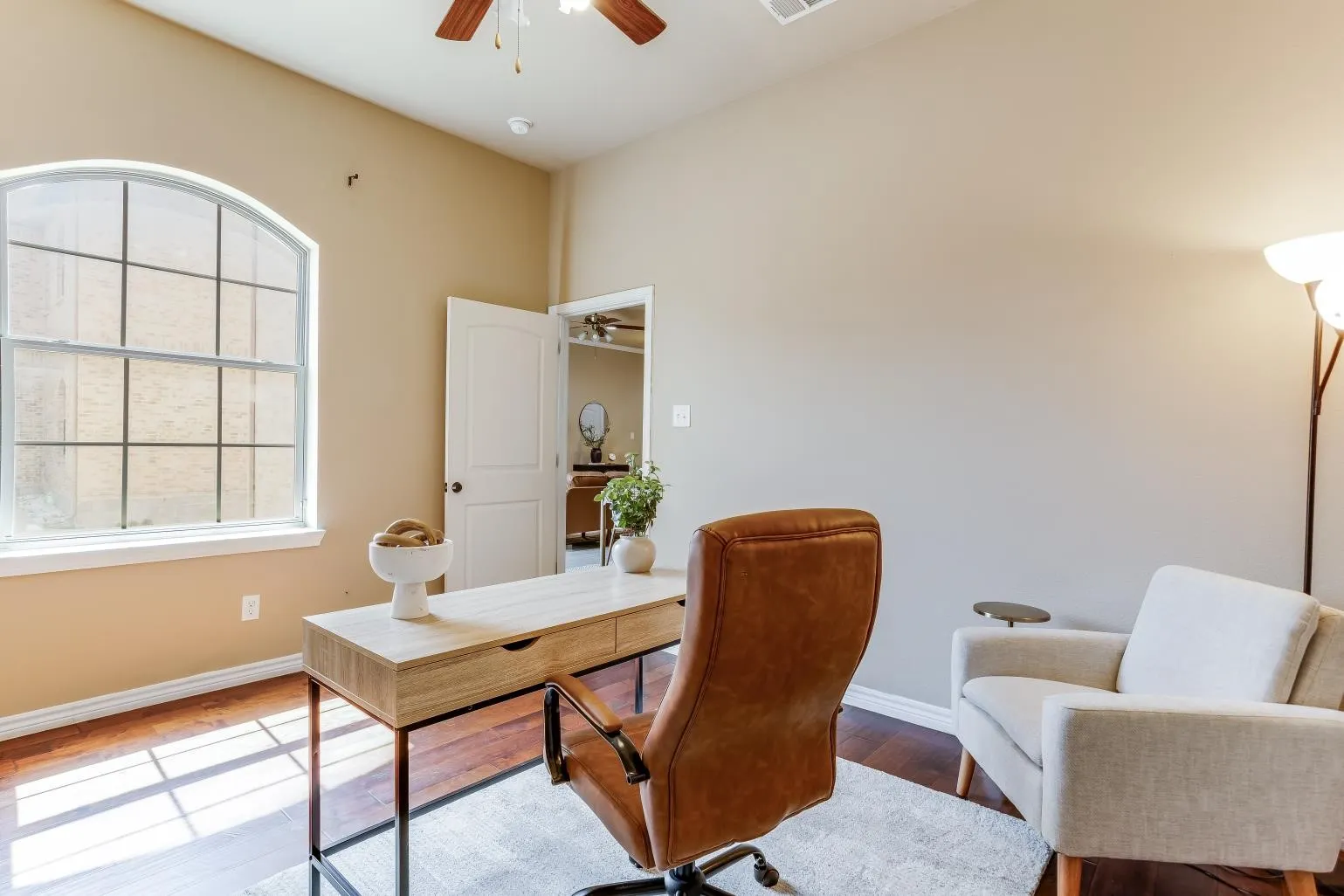 Arch-top window with grid detailing, rich wood-finish flooring, and ceiling fan with integrated lighting