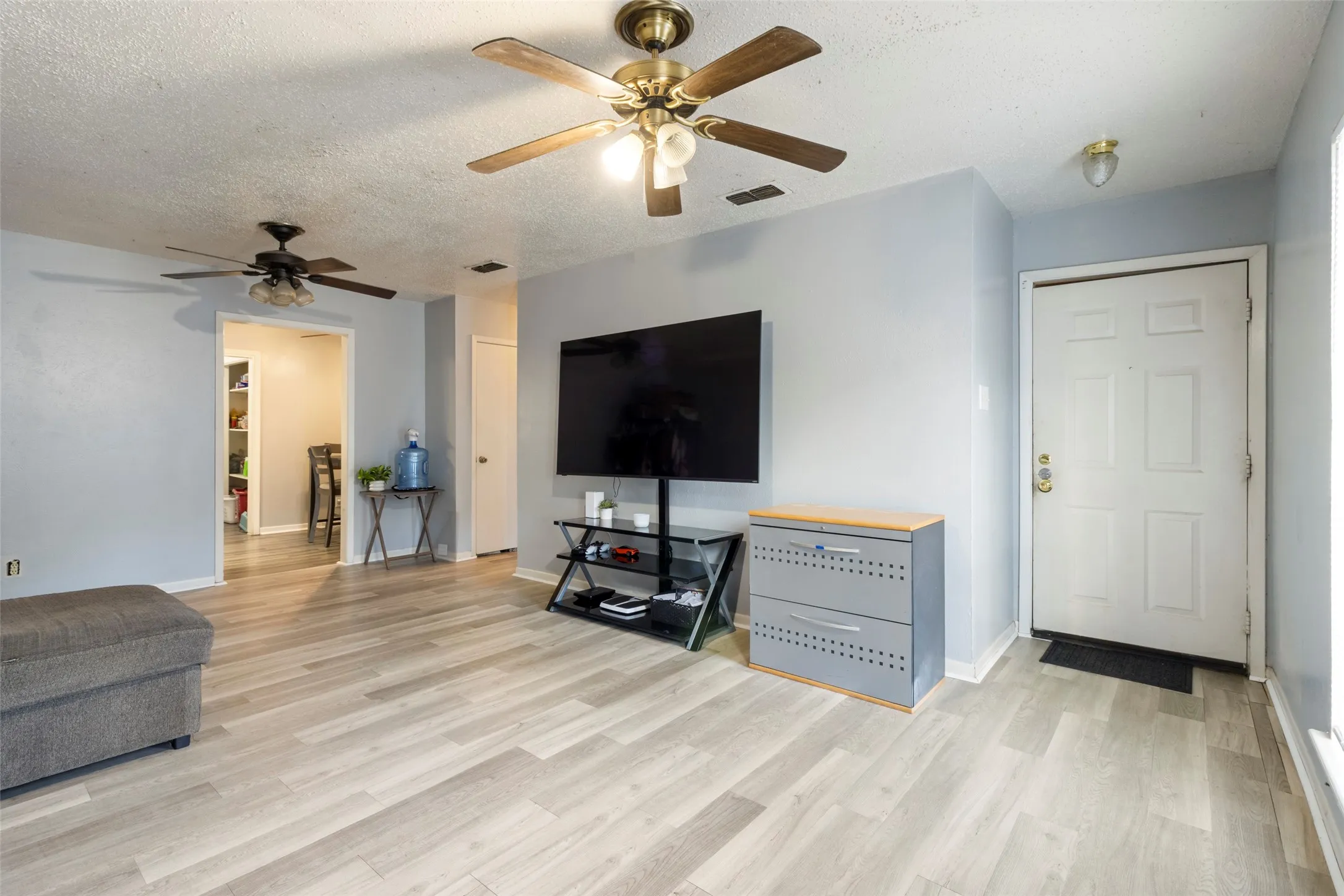 Wood-finish flooring throughout, ceiling fans with integrated lighting, and a paneled entry door