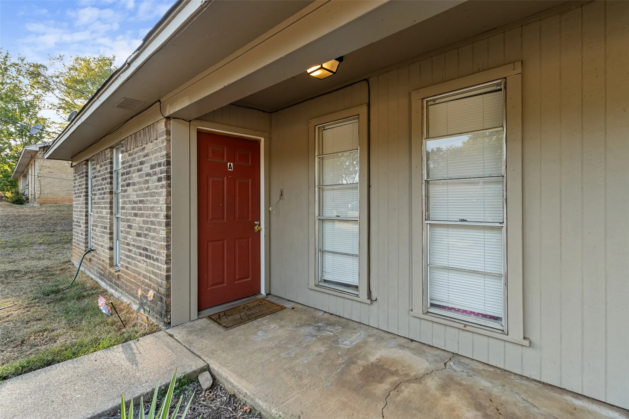 Brick exterior with a covered entryway, red paneled door, and two vertical windows