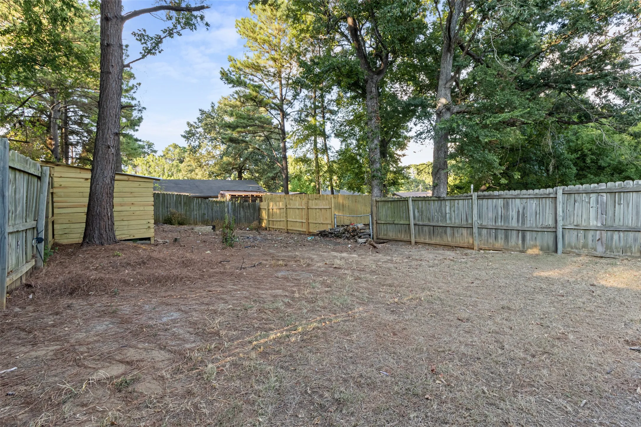 Spacious yard featuring mature trees, a new wooden storage shed, and perimeter fencing