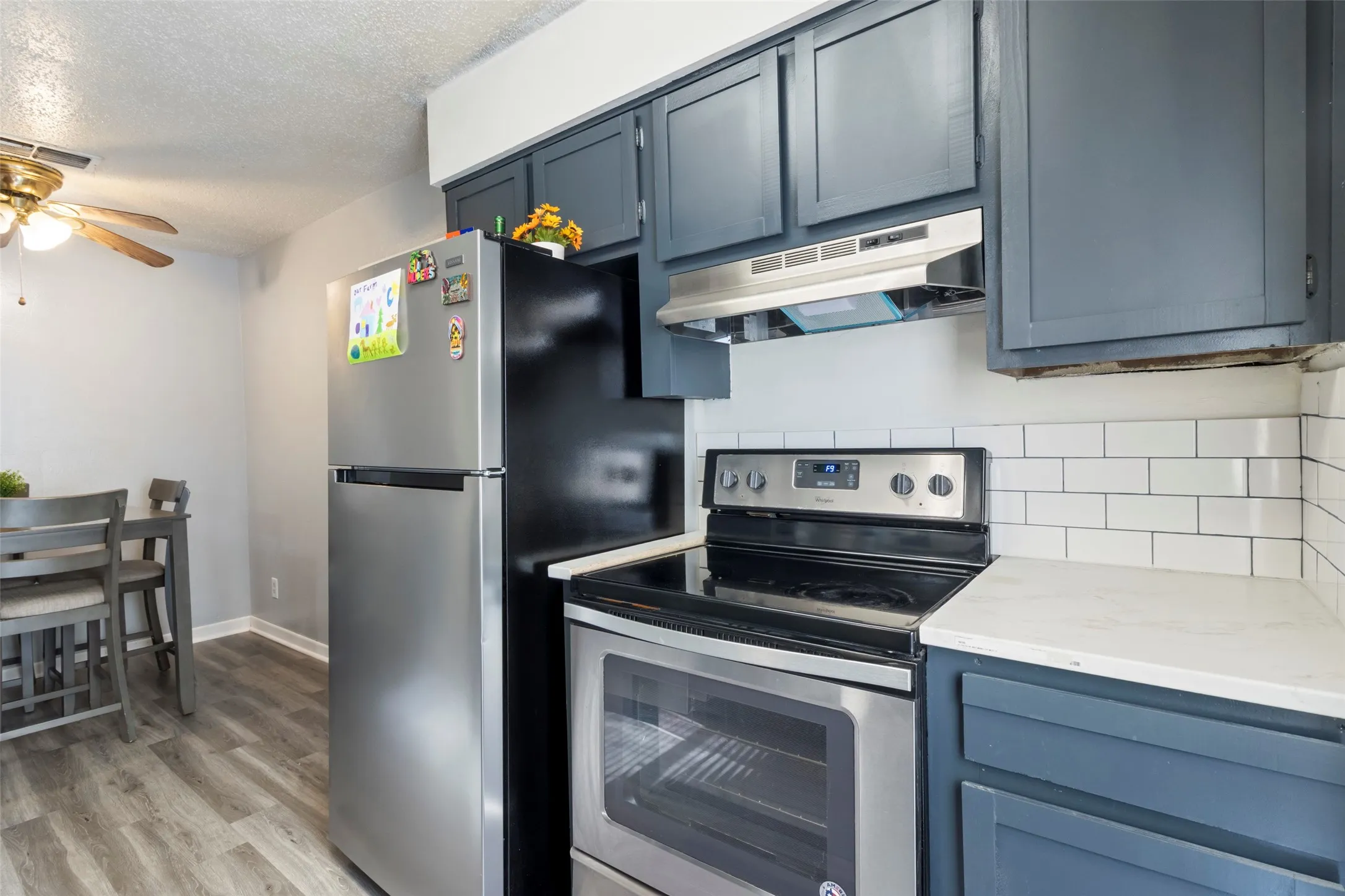 Kitchen featuring wood-finish flooring, white subway tile backsplash, dark-painted cabinetry, white countertops, and stainless steel appliances