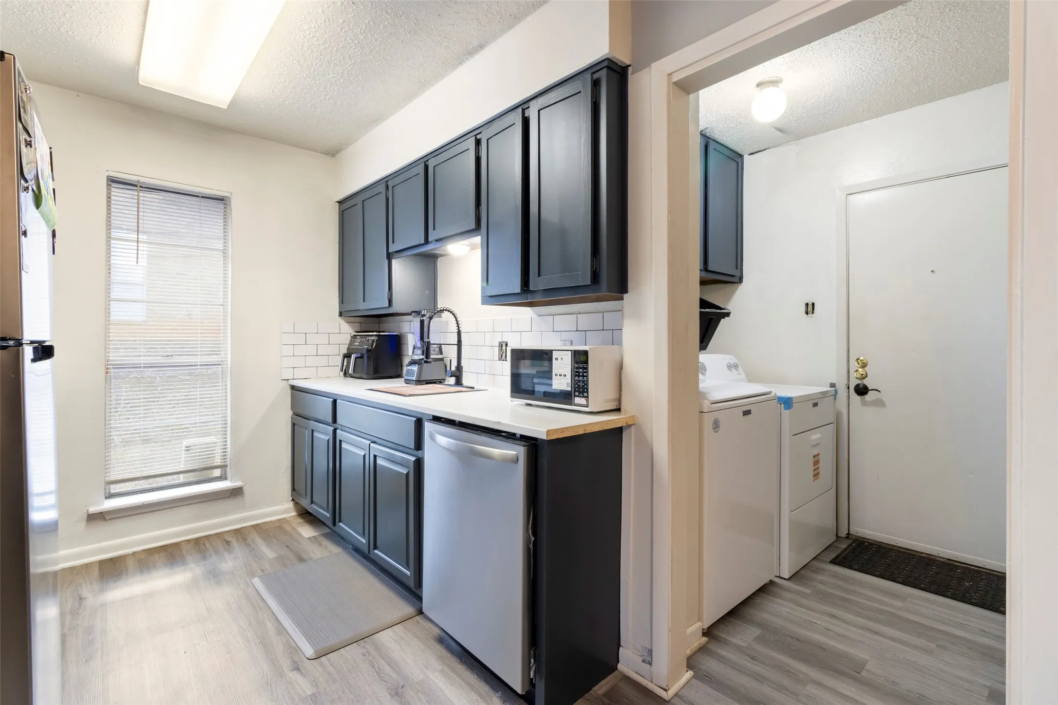 Kitchen featuring wood-finish flooring, dark cabinetry, white subway tile backsplash, and a stainless steel dishwasher