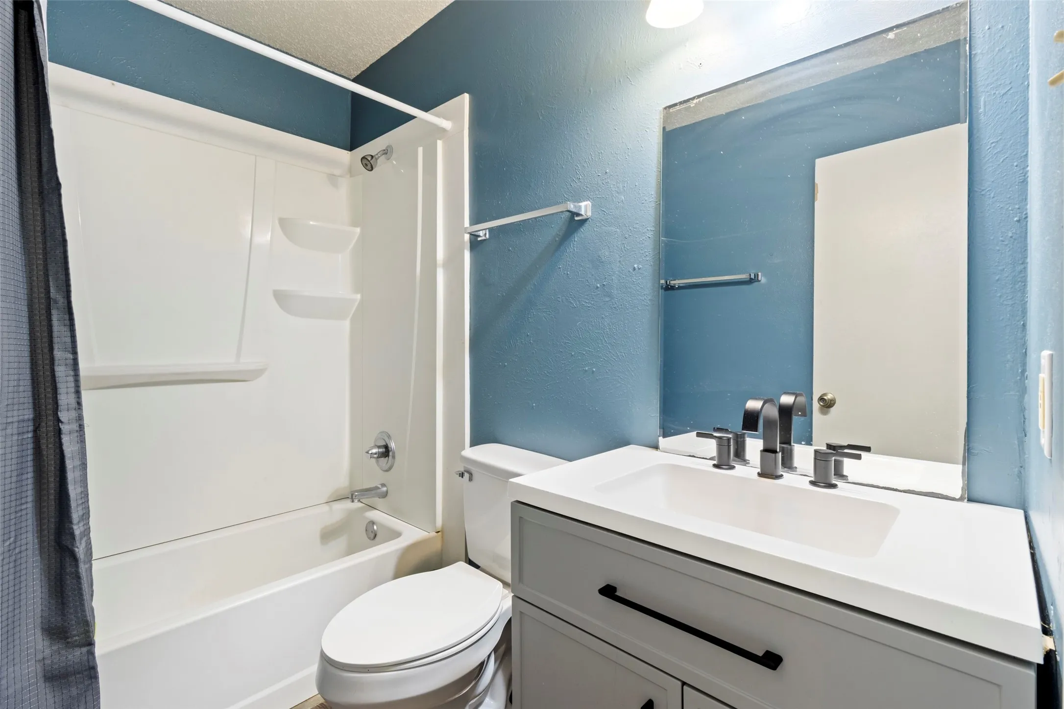 White shower/tub combination with built-in shelving, gray vanity with white countertop, and dark-finish fixtures