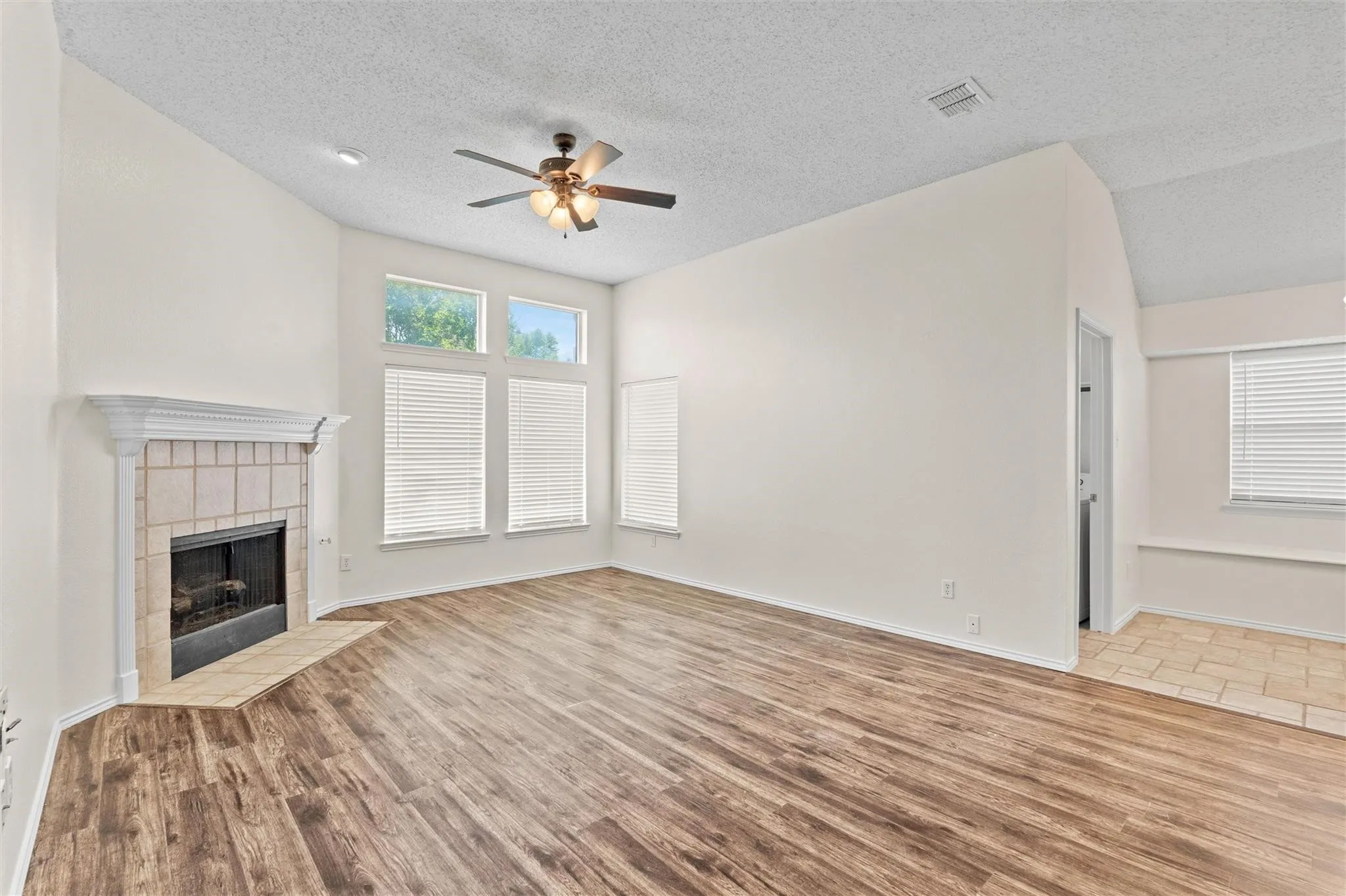 Vaulted ceilings with a ceiling fan, wood-finish flooring, and a tiled fireplace with a mantel