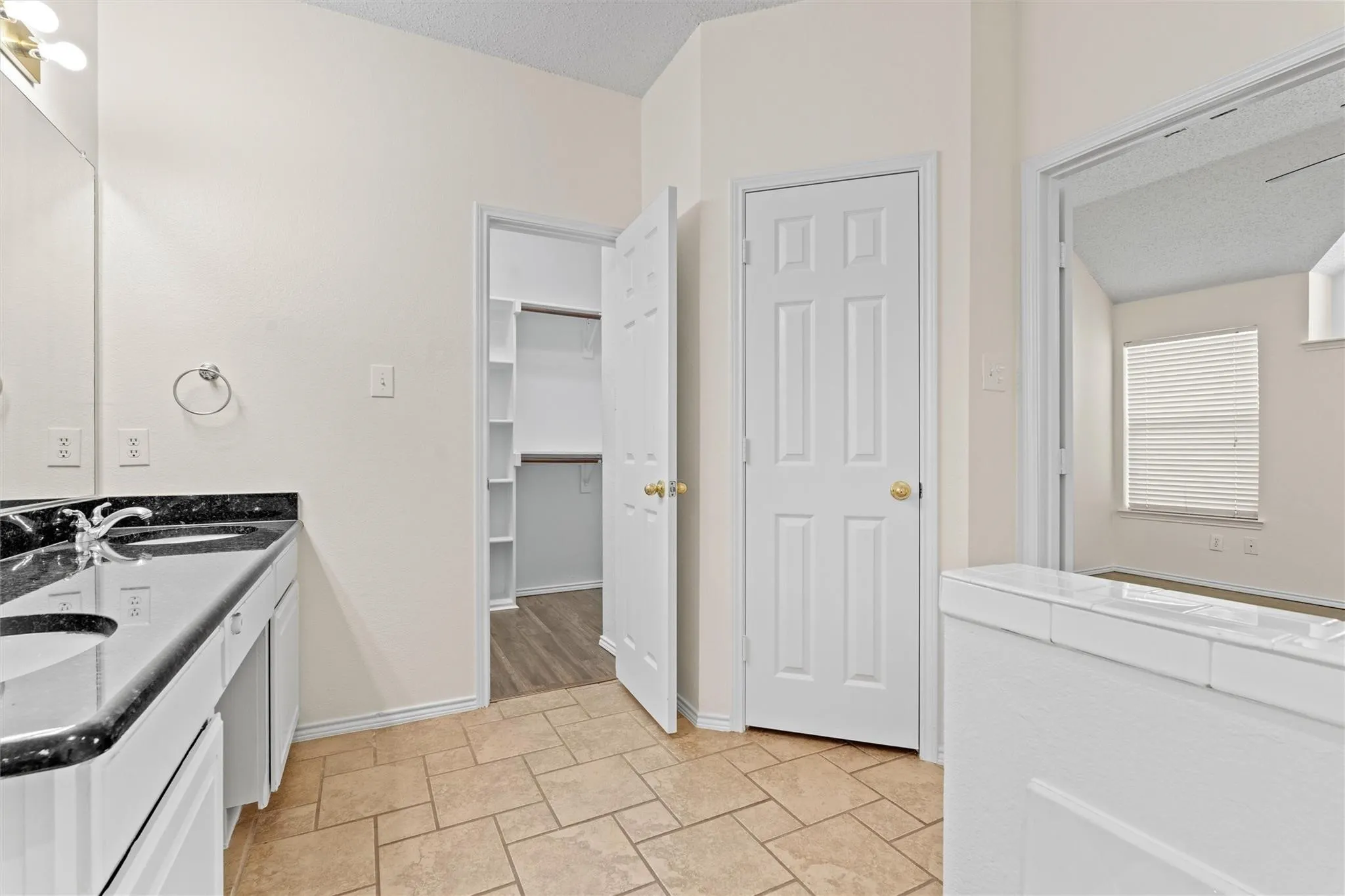 Double vanity with dark stone countertops, tile flooring, and a walk-in closet with built-in shelving