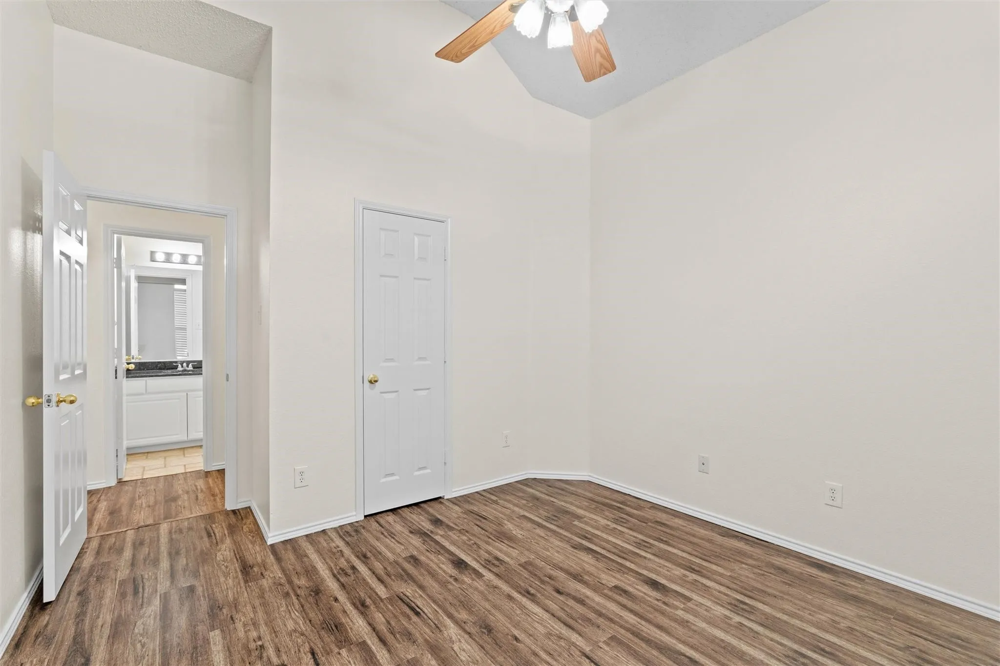 Vaulted ceiling with a ceiling fan, wood-finish flooring, and white interior doors